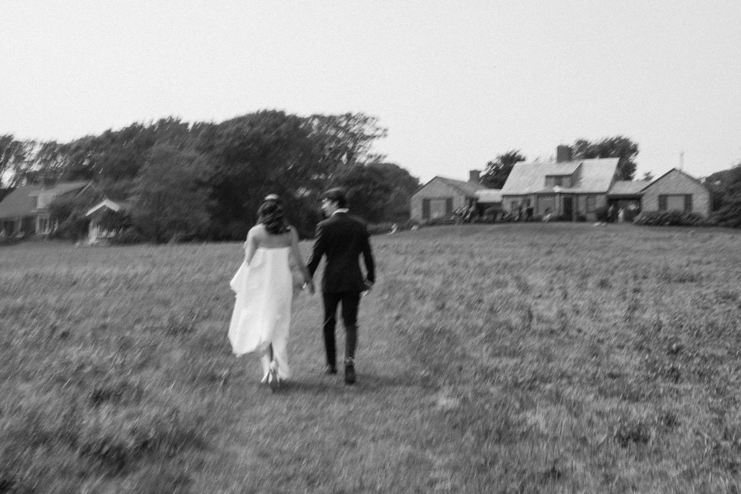 Newlyweds stroll hand in hand across a grassy hillside landscape.
