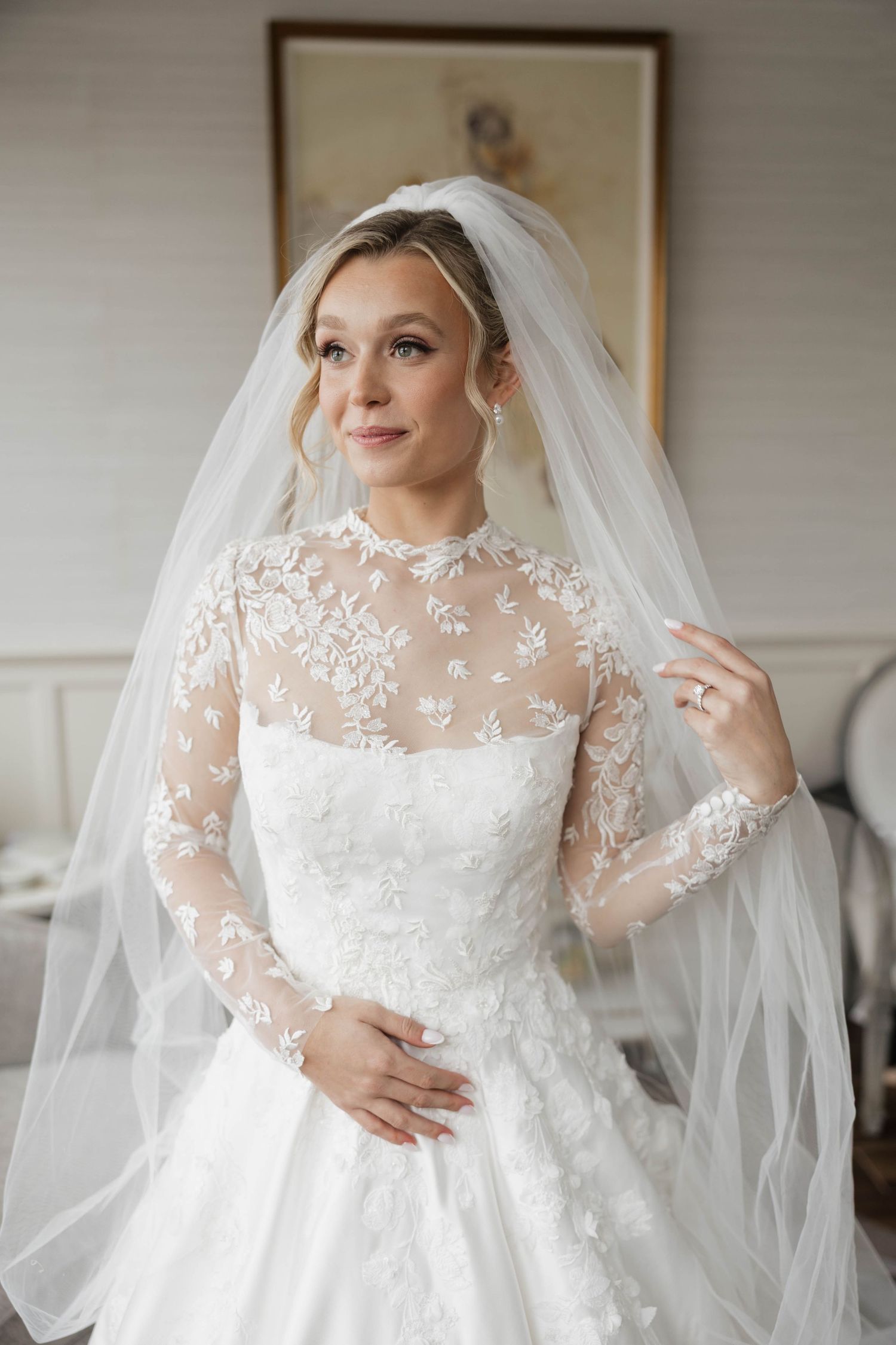 Detailed lace wedding dress with sheer long sleeves and flowing veil captured in elegant bridal portrait.
