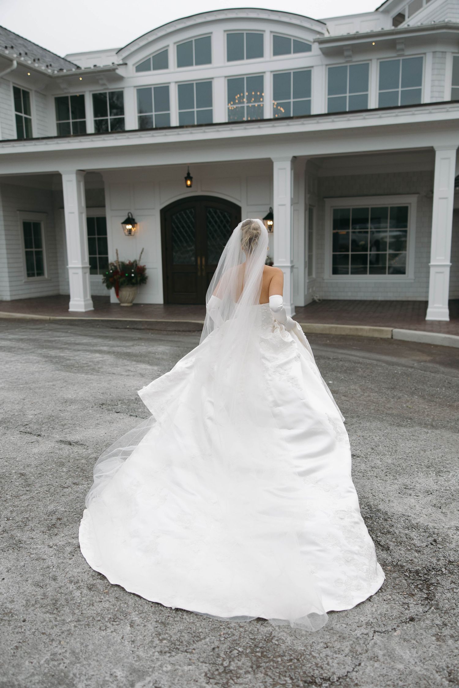 A bride's white ballgown dress billows dramatically in front of an elegant white venue entrance.