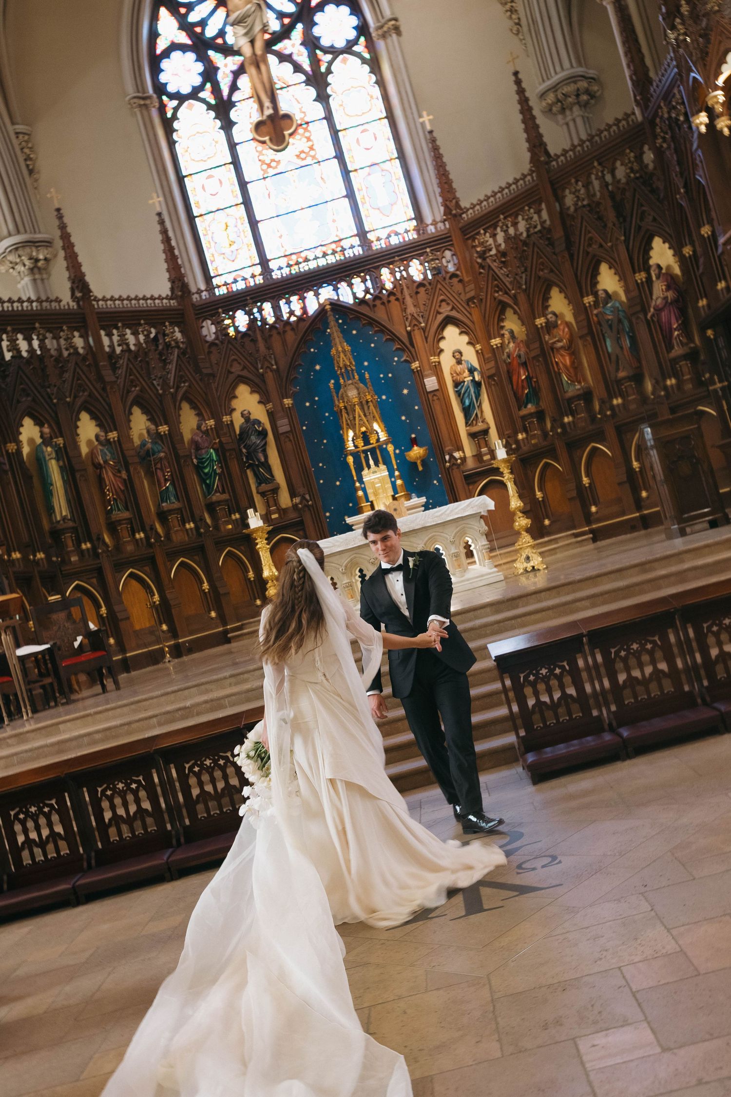 Bride and groom dance at ornate church altar with intricate Gothic woodwork and stained glass backdrop.