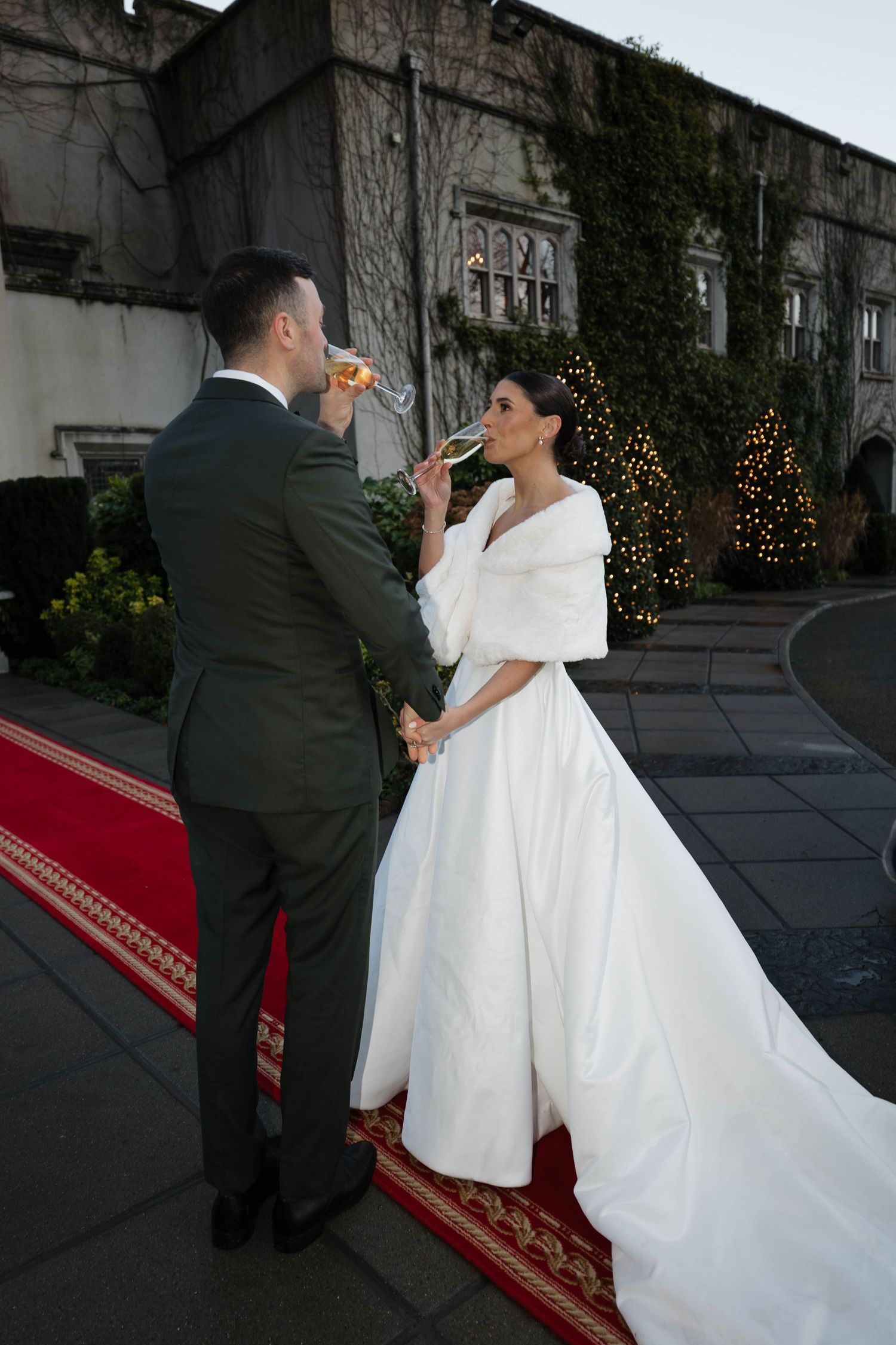 Newlyweds sharing a drink outside historic stone building with red carpet.