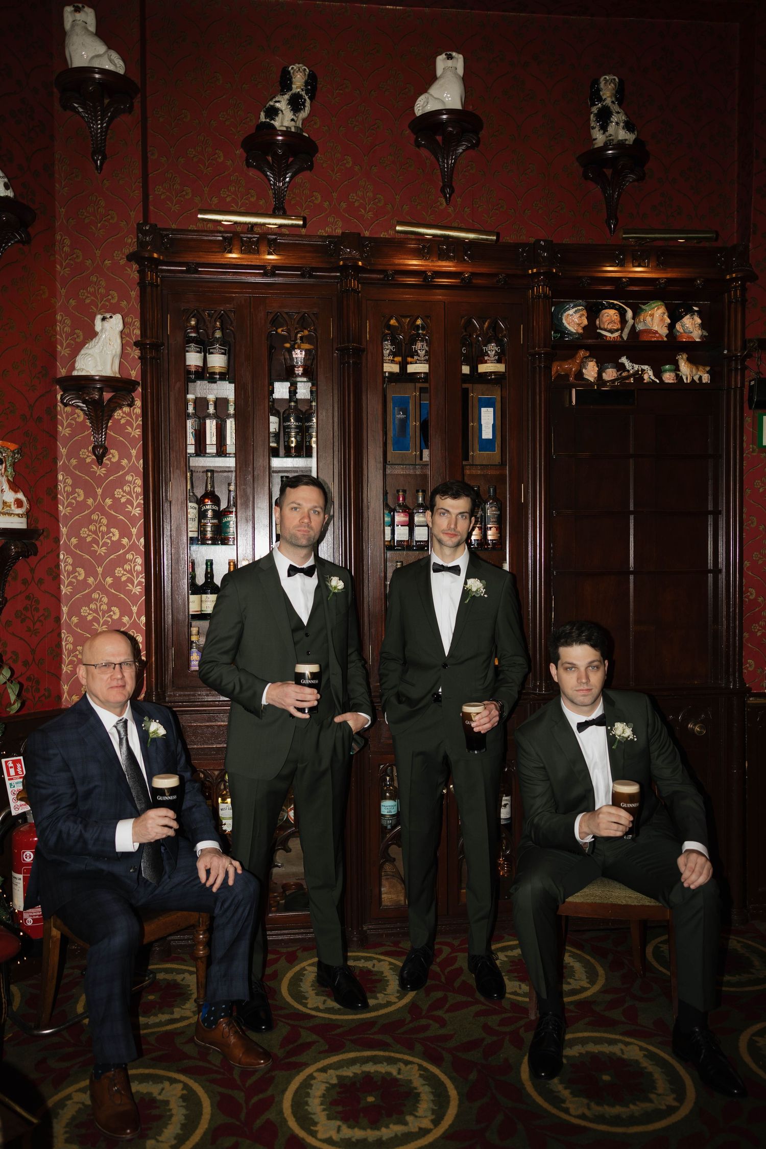 Groomsmen in formal attire pose together in front of wooden bar cabinets.
