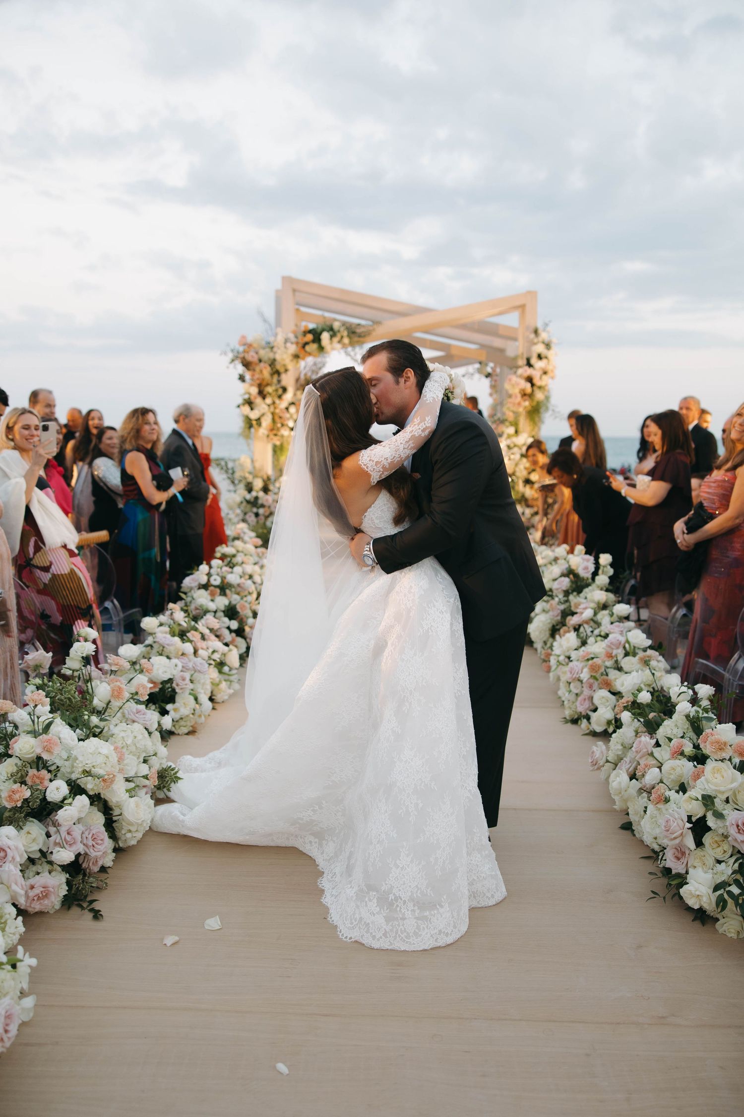Joyful wedding ceremony moment on a beachfront deck with floral-decorated white pergola.