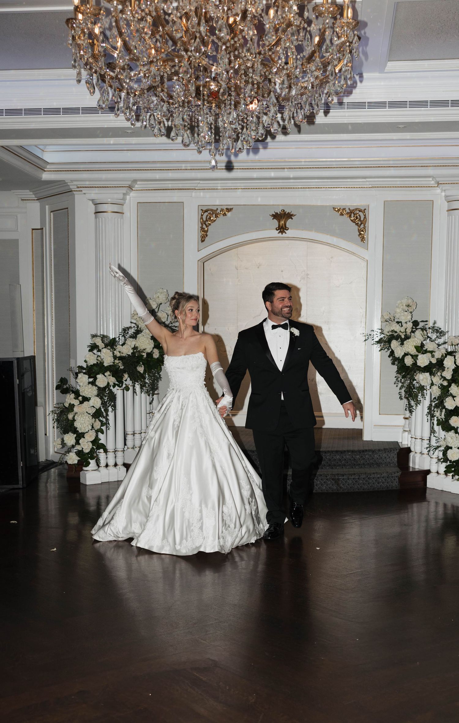 Newlyweds making their grand entrance under a crystal chandelier in an elegant ballroom.