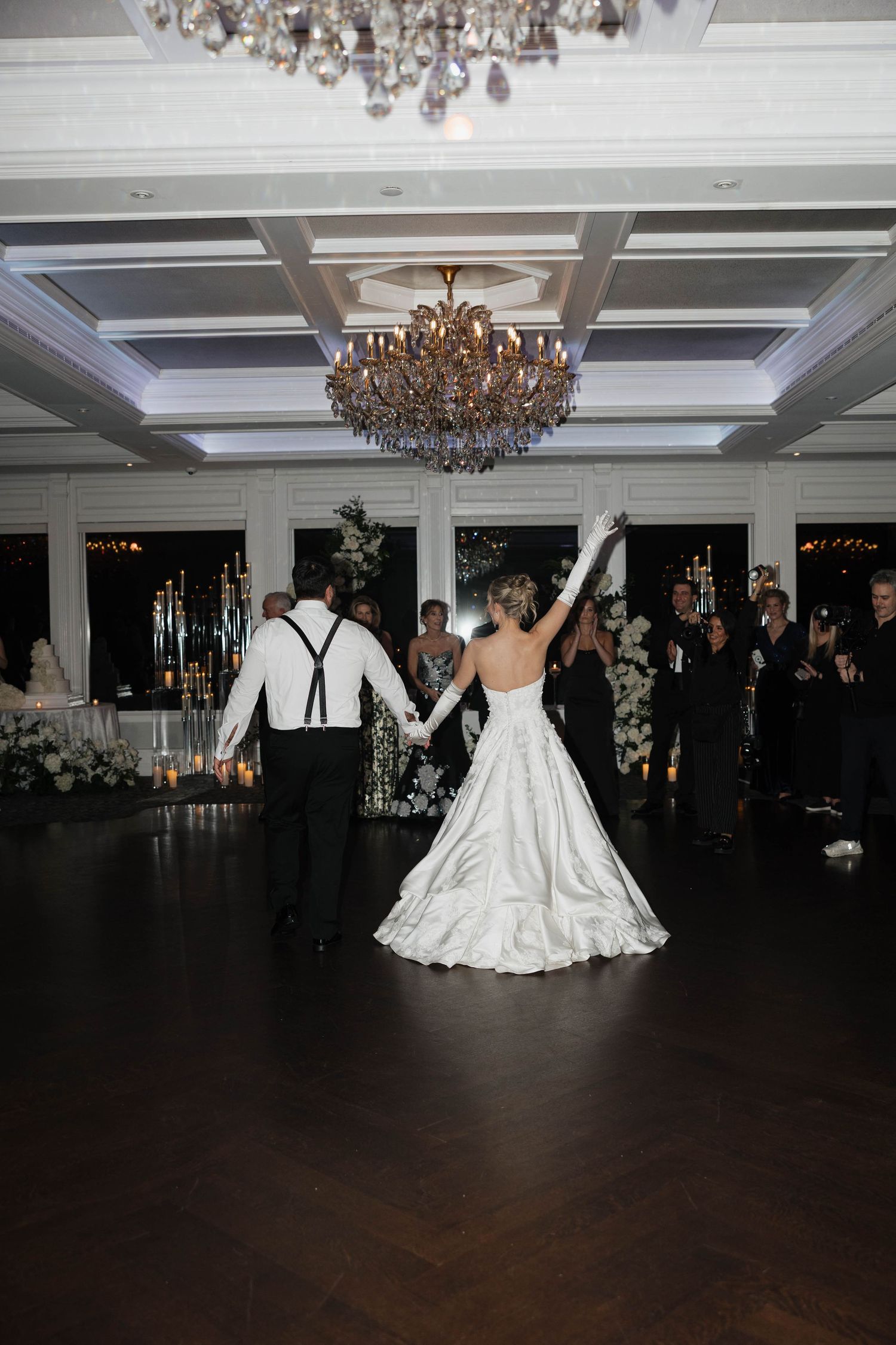 Wedding reception dance floor scene with chandeliers and elegant white decor.
