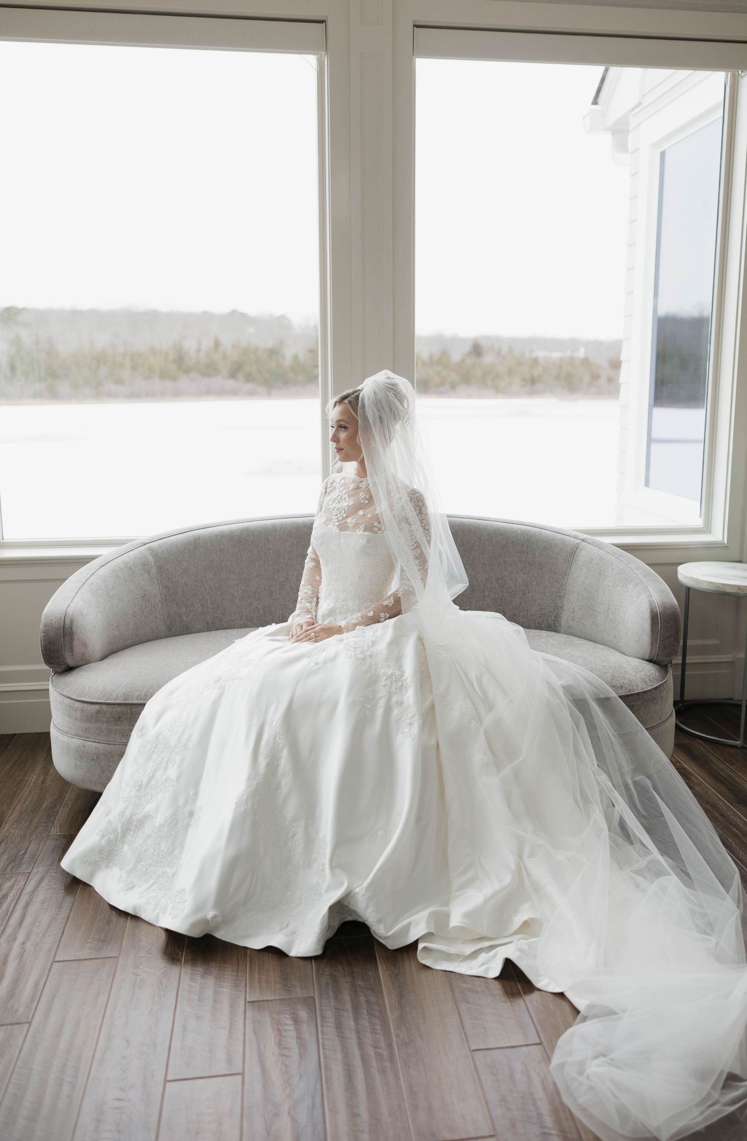 Wedding gown with dramatic train spread across wooden floor in bright interior setting.
