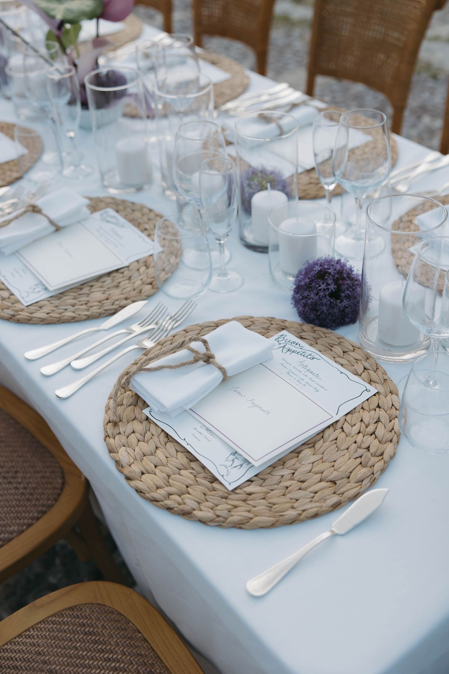 Elegant table settings with woven placemats, white linens, and purple floral accents.