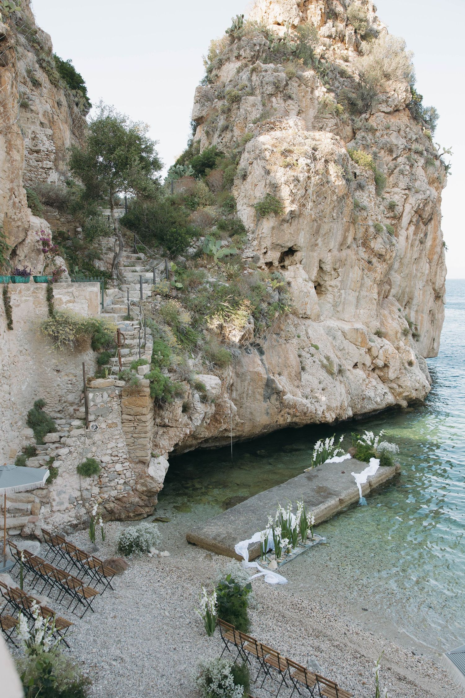 Elegant beach wedding venue with stone cliffs, turquoise waters, and wooden ceremony seating.