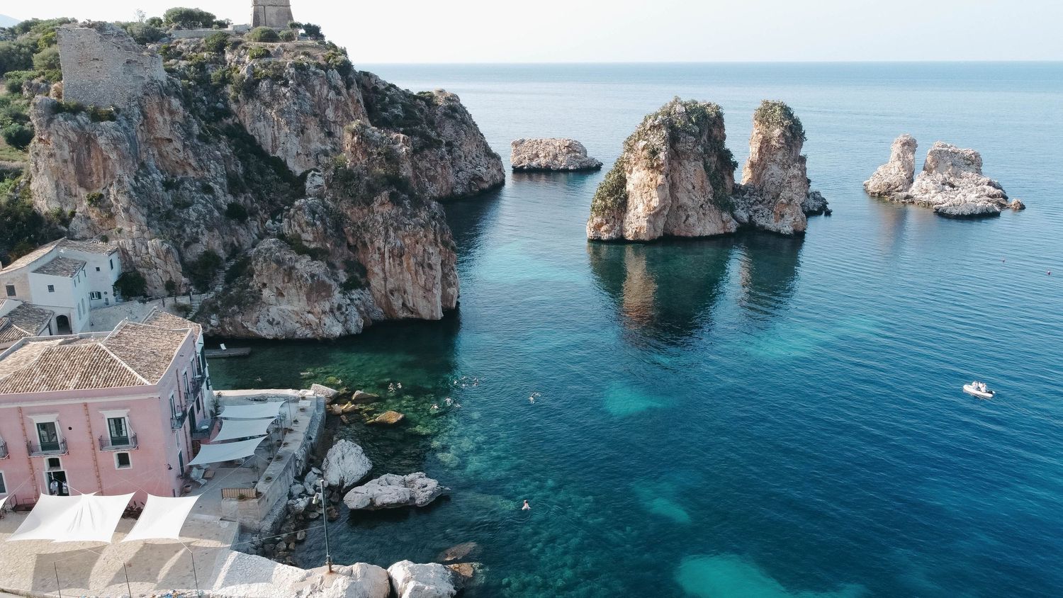 Wide angle view of Mediterranean cove with pink buildings perched on dramatic coastal cliffs.