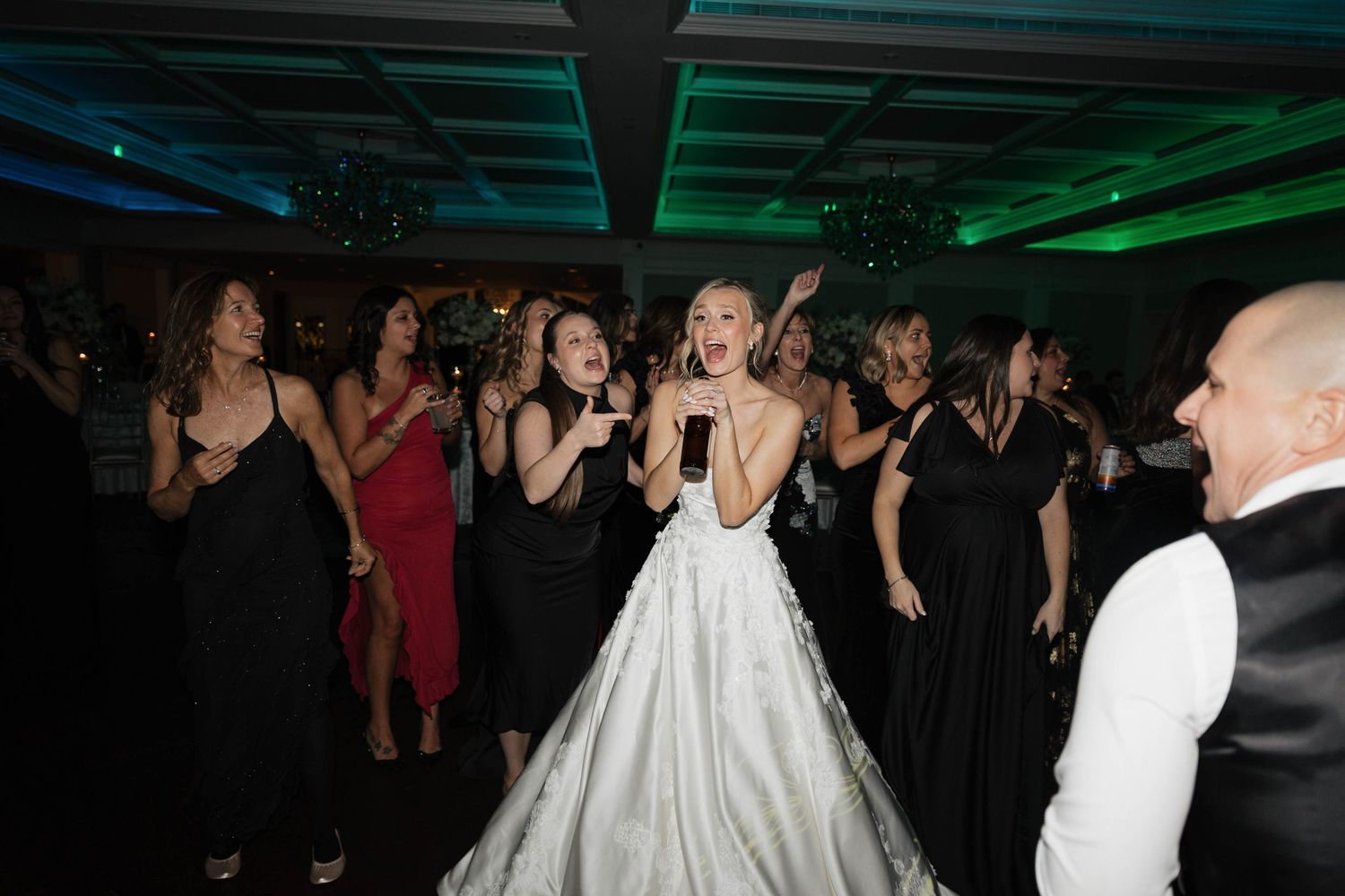 Wedding guests enjoying the dance floor under atmospheric blue and green lighting effects.