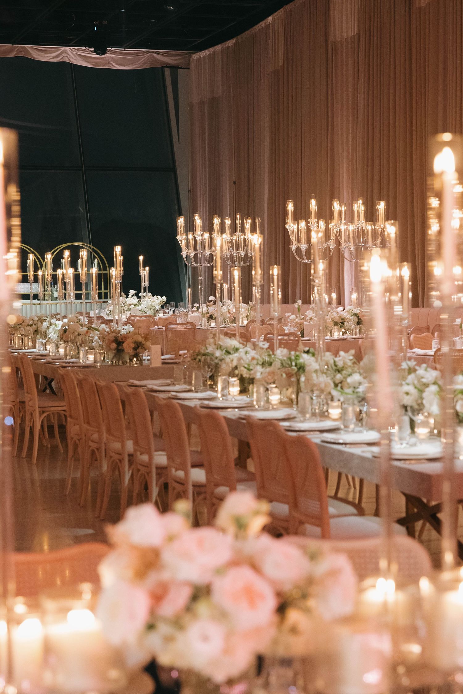 Long reception table with crystal chandeliers and pink chairs creating a romantic ambiance.
