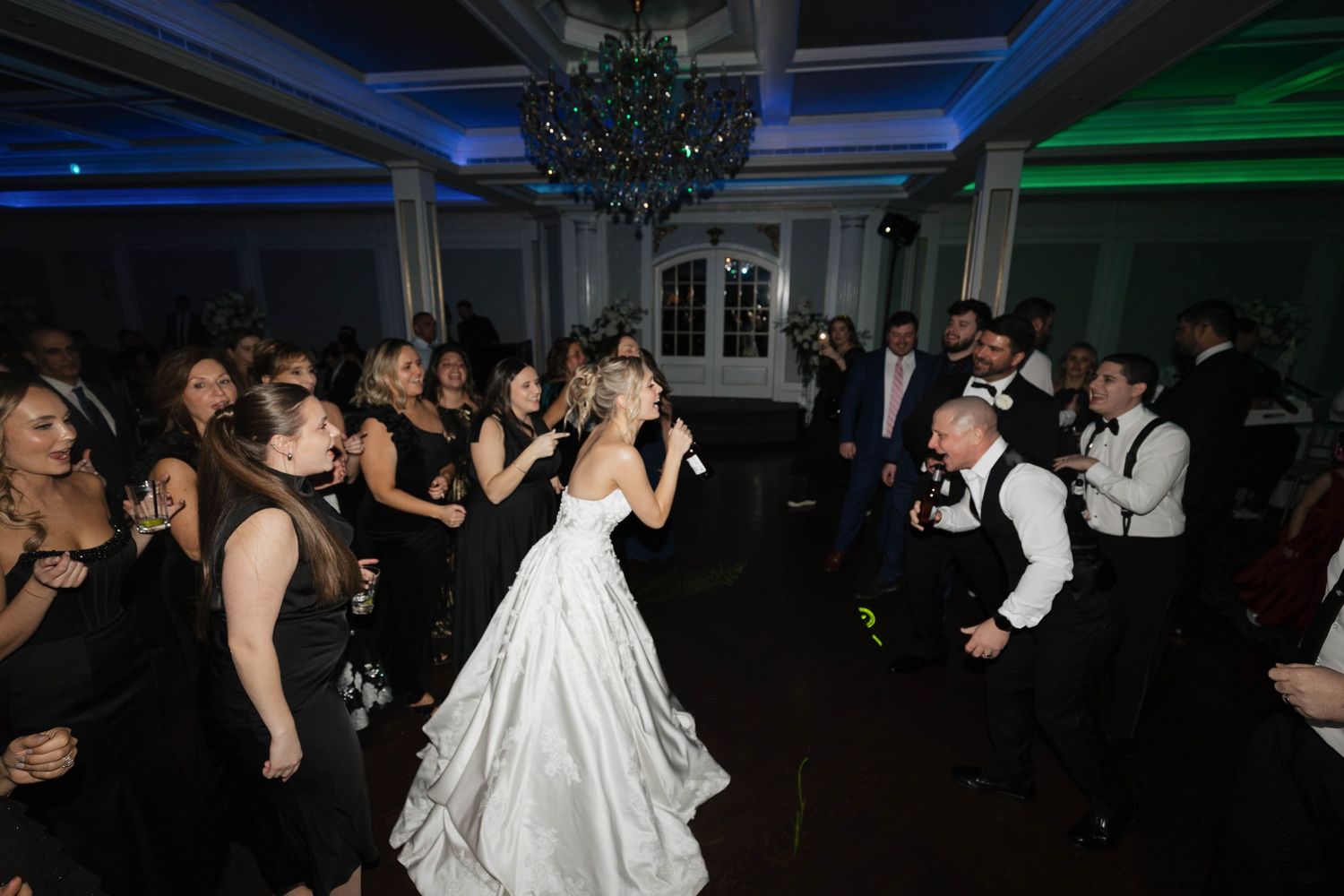 Wedding reception dance floor filled with guests dancing under blue and green lighting.