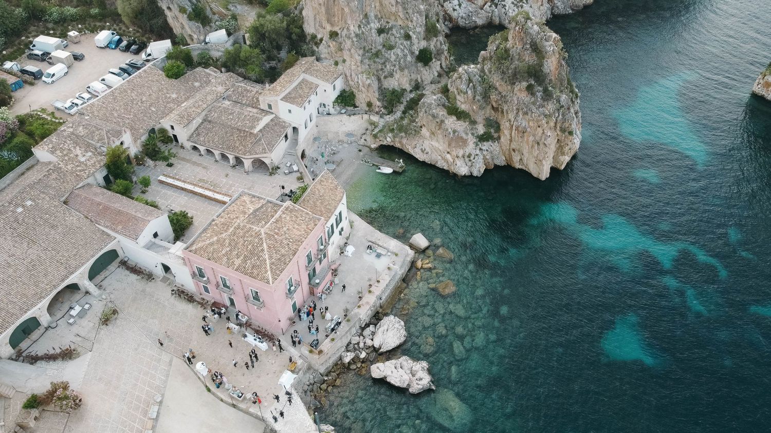 Sweeping aerial view of Mediterranean architecture along dramatic rocky coastline.