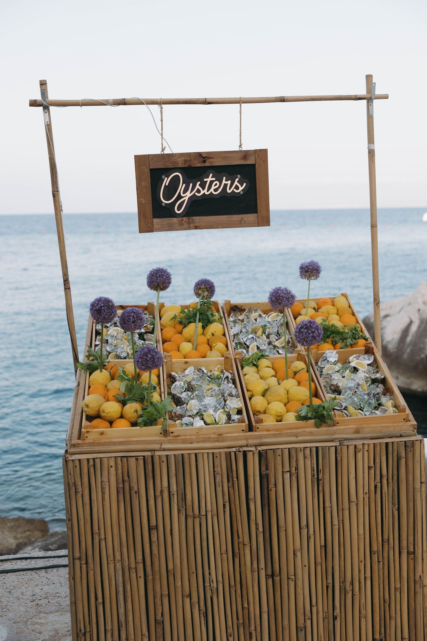 Rustic bamboo display stand with fresh oysters and lemons at a beachside event.