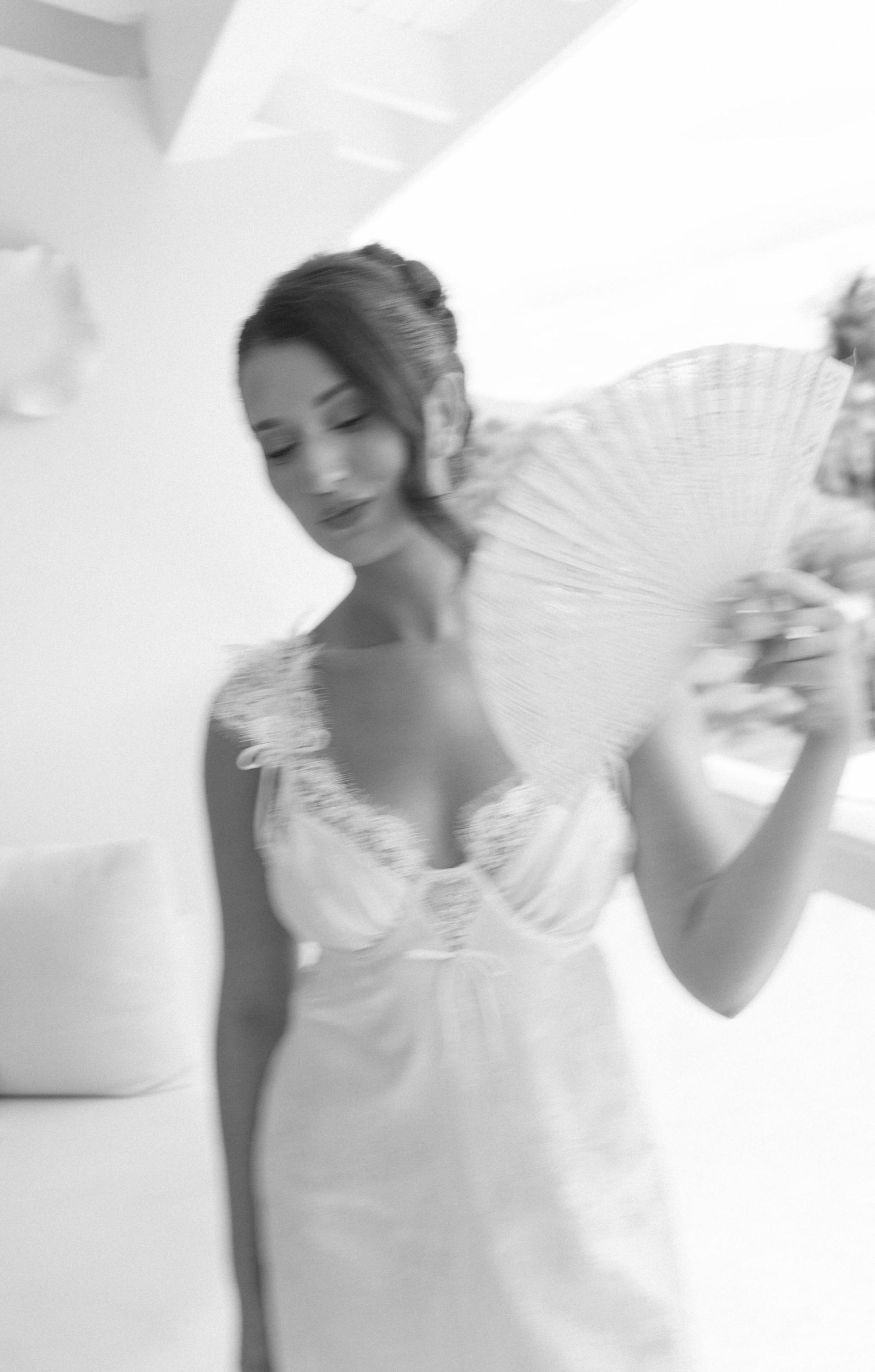 Black and white photo of a bride in a white gown holding an elegant hand fan, looking down gracefully.