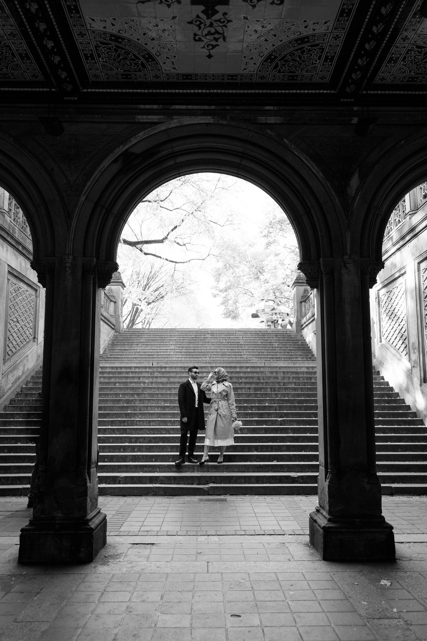 Black and white sequence under stone archways showing silhouettes on grand staircase.