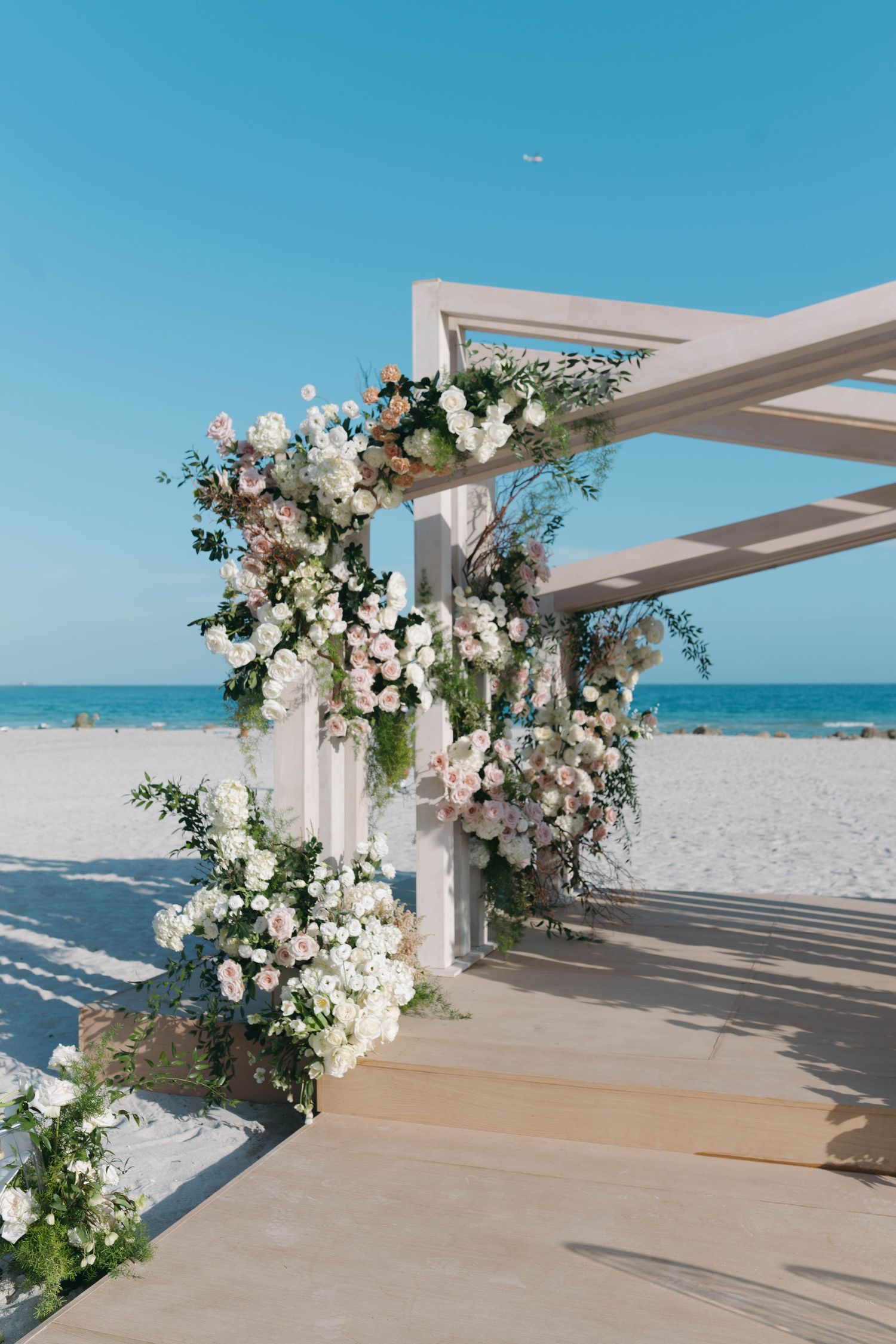 Coastal wedding ceremony space with modern white arch decorated in luxurious florals.