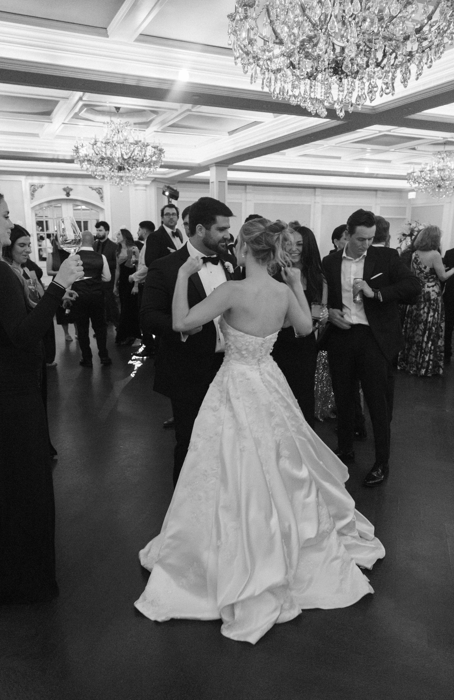 Wedding celebration on dance floor under crystal chandeliers in elegant ballroom setting.