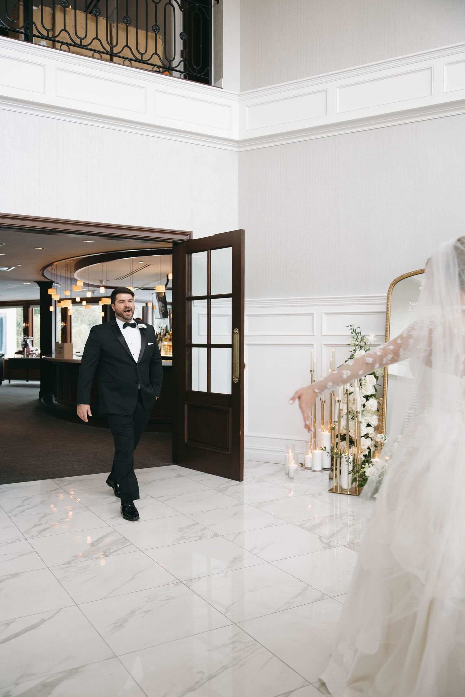 A first look wedding moment captured in an elegant white interior with marble floors and gold accents.