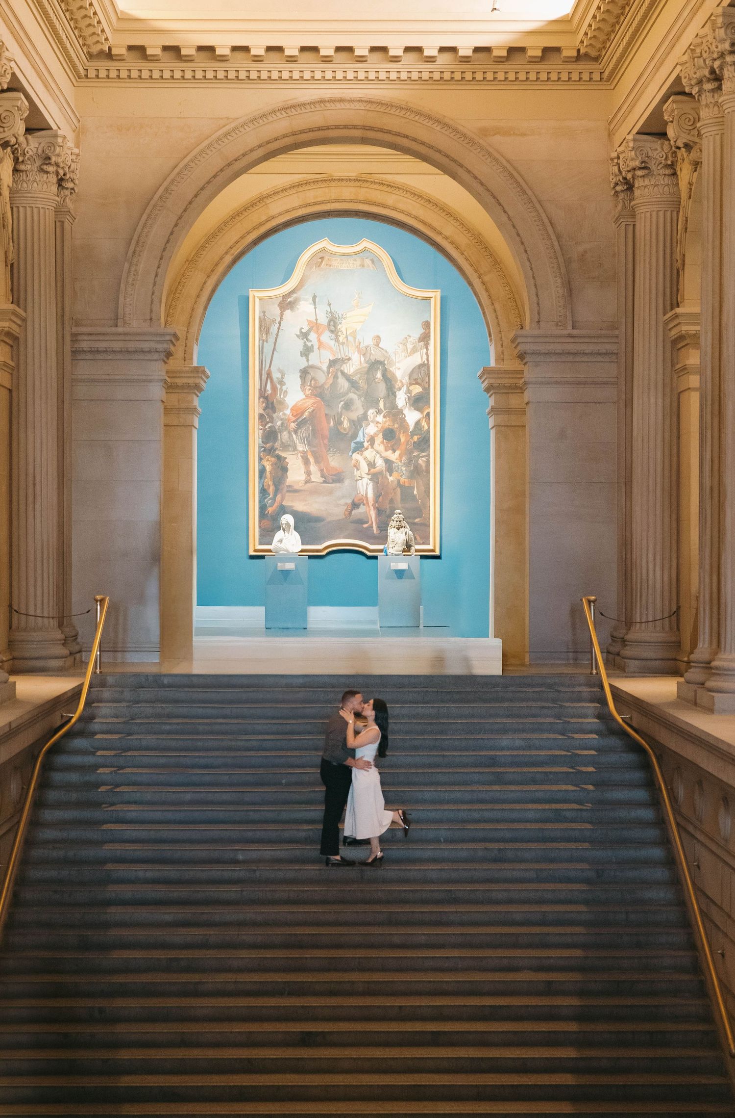 Grand architectural interior with blue alcoves and sweeping staircase capturing romantic moments.