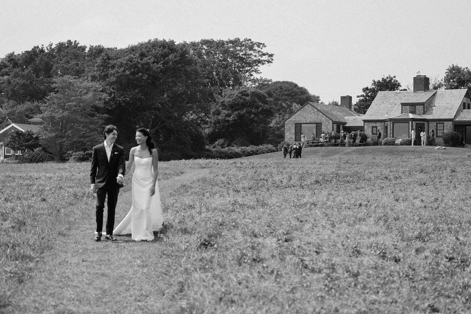 Wedding couple stands in a scenic field with a building in the distant background.