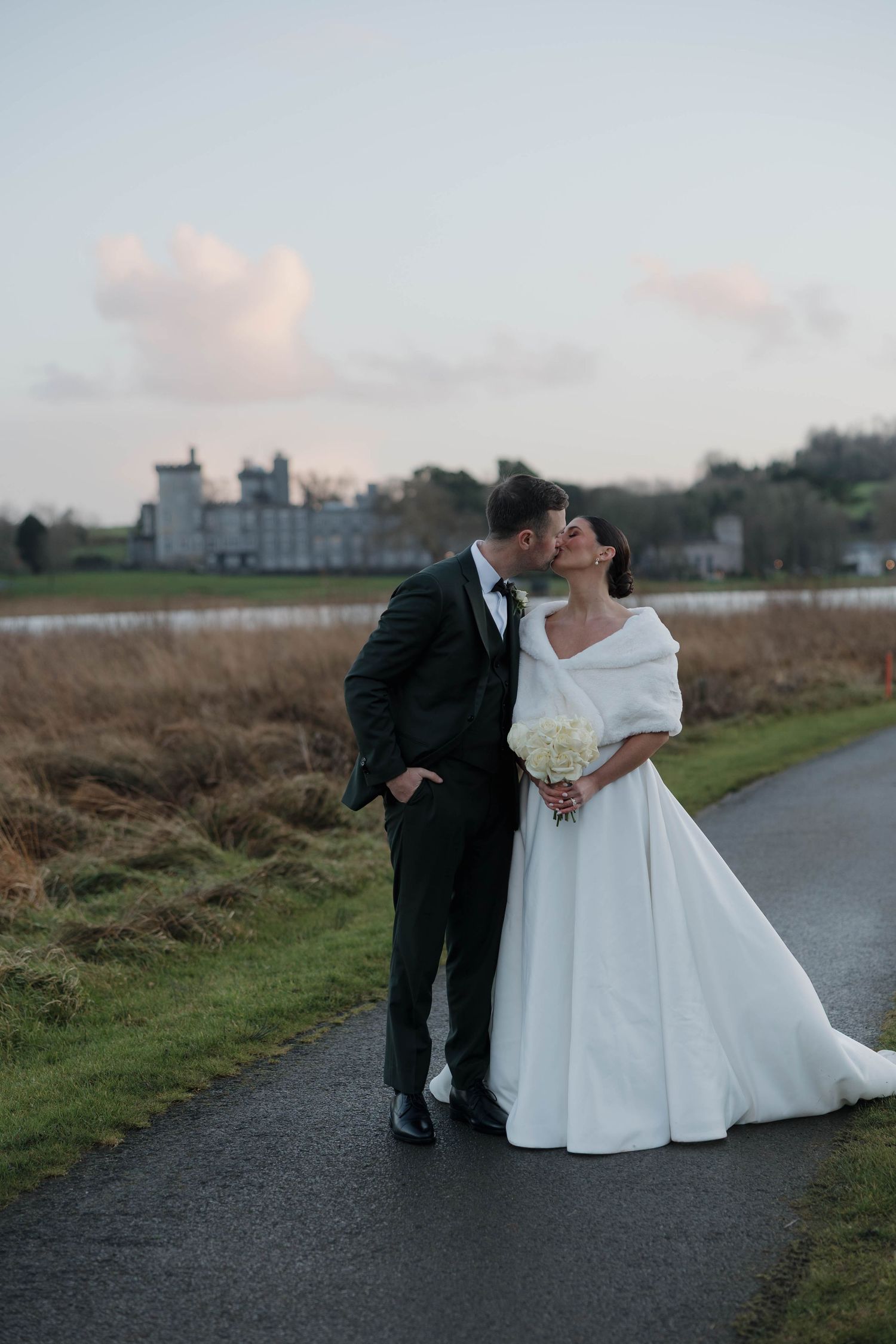 Wedding couple shares intimate moment on path with castle in background.