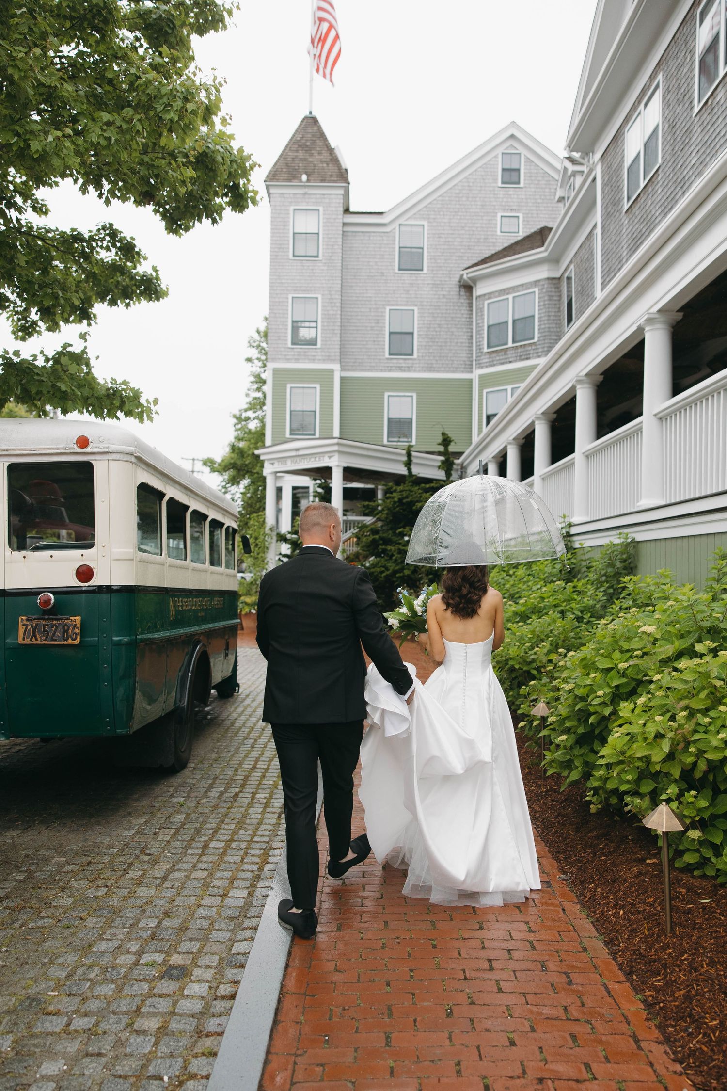 Wedding couple walks down brick pathway past American flag at Nantucket hotel.