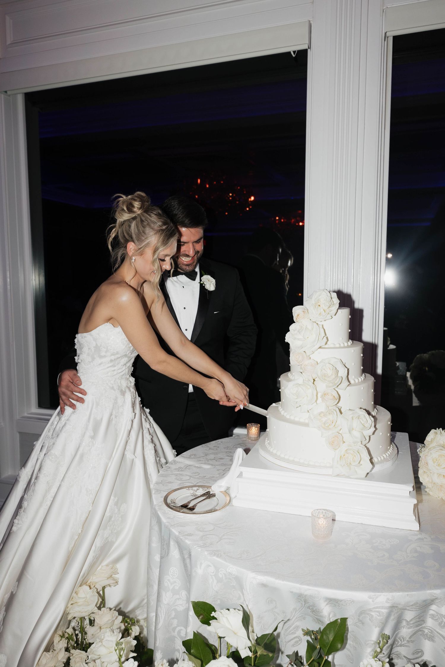 Wedding couple sharing a moment while cutting their tiered white cake at a formal reception.