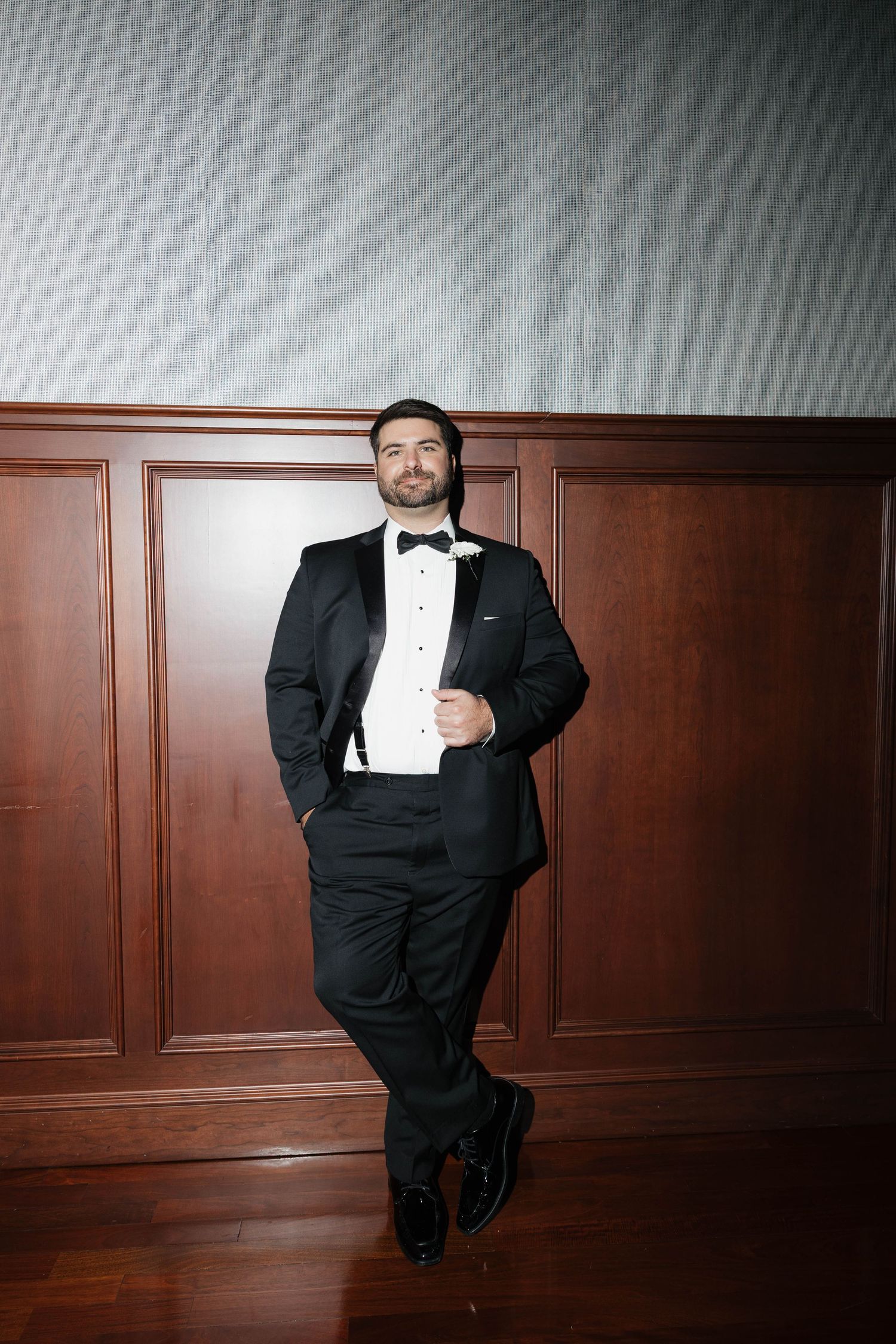 Dramatic low-angle portraits of a groom in formal attire against wood paneling.