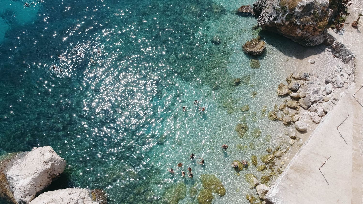 Close-up aerial view of pristine turquoise Mediterranean waters meeting rocky coastline.