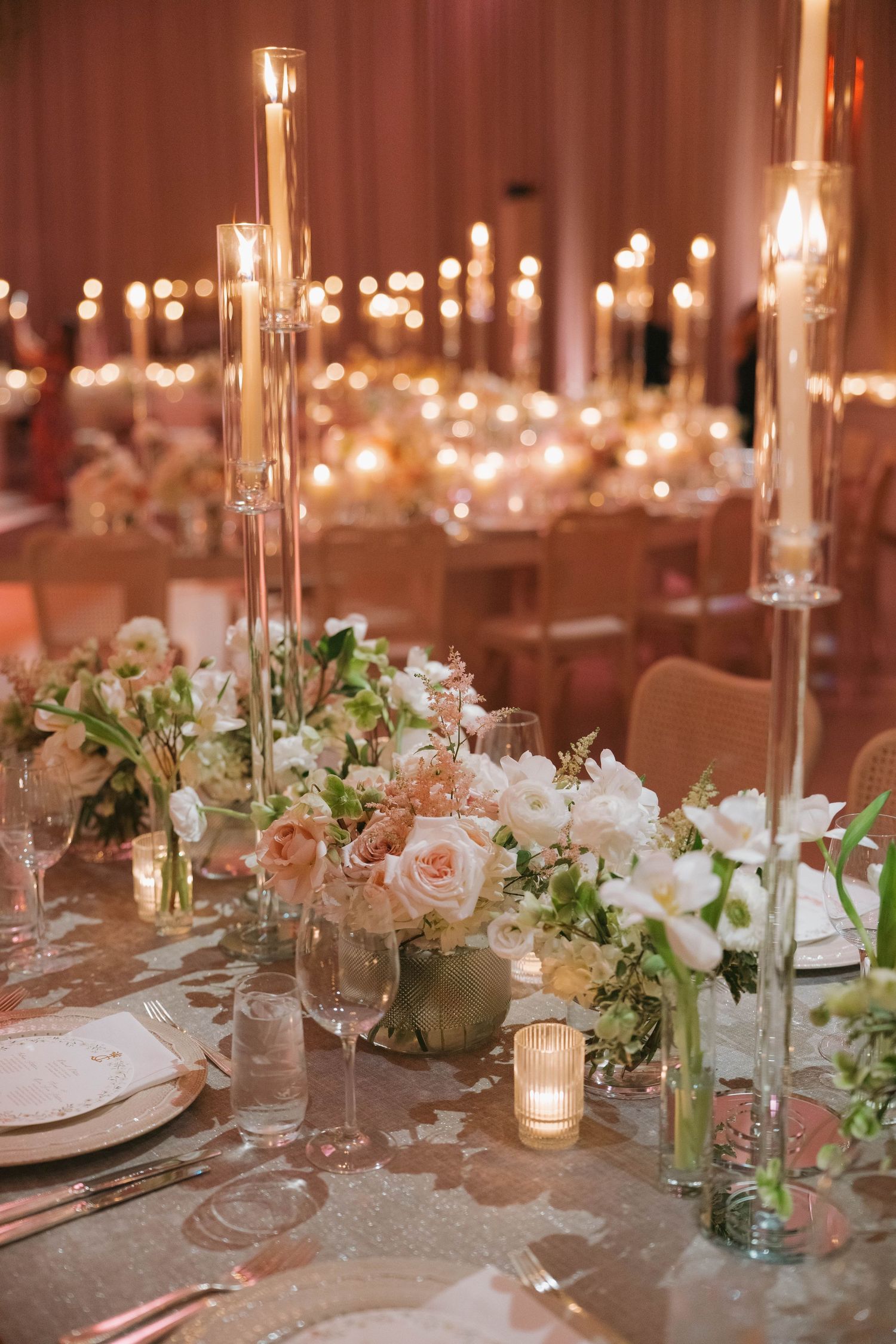 Romantic table settings with white floral arrangements, candles, and crystal stemware creating an intimate atmosphere.