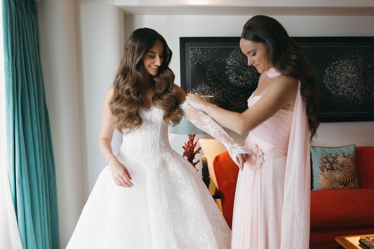 Two people preparing a wedding dress in a room with turquoise curtains.