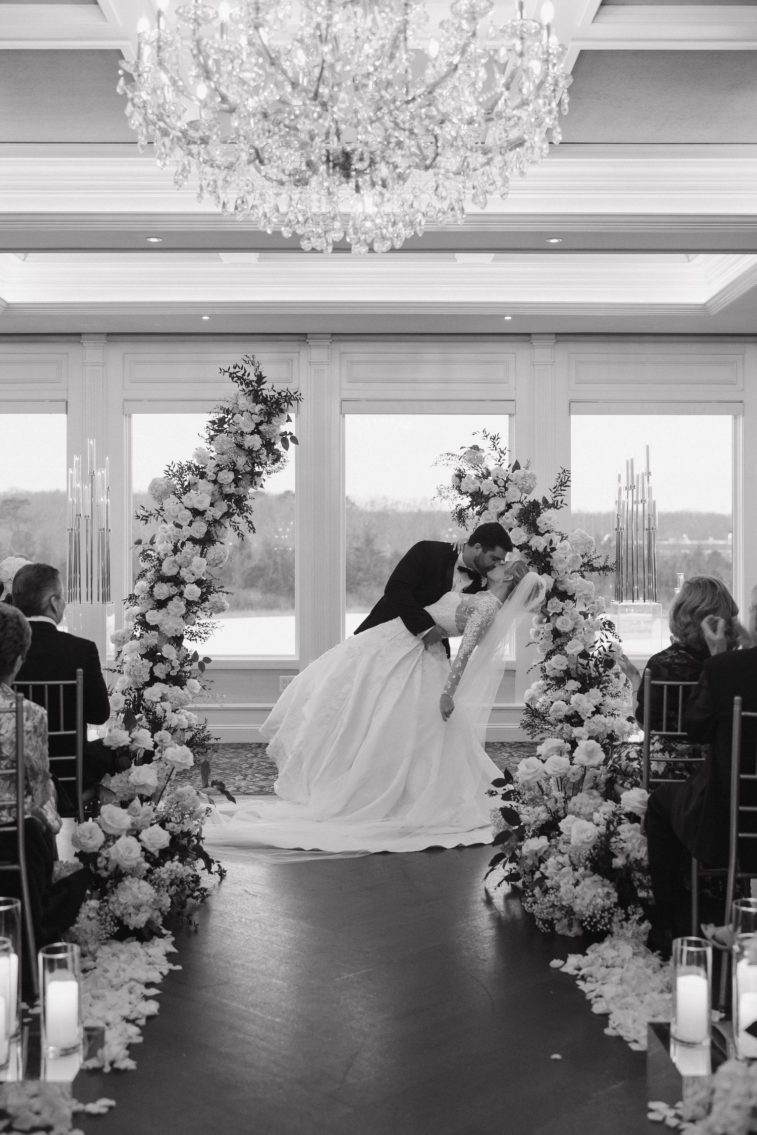 Black and white wedding photo showing couple's romantic moment under crystal chandelier.
