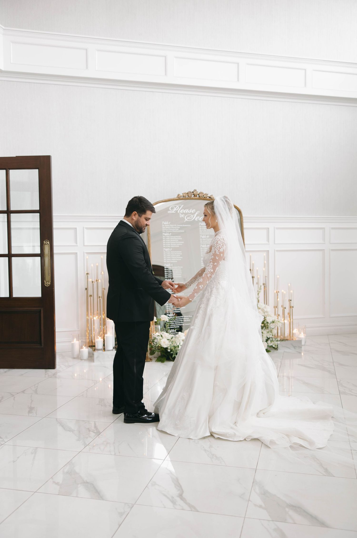 Wedding couple sharing an intimate moment in an elegant white room with candles and flowers.