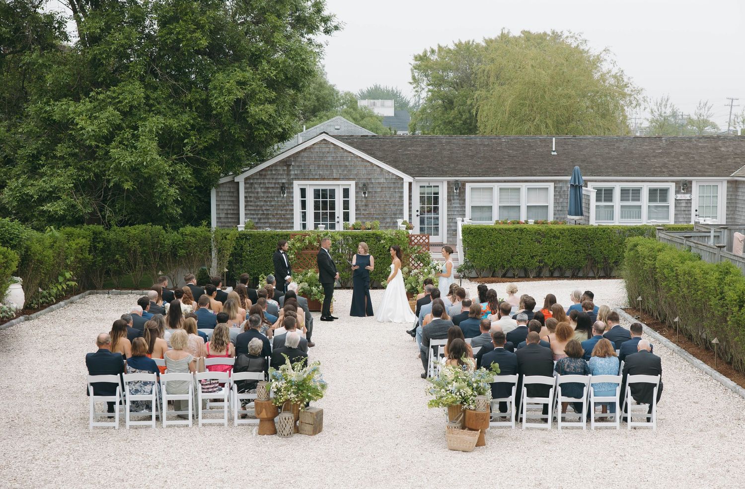 Wide view of outdoor wedding ceremony with guests seated on white chairs.