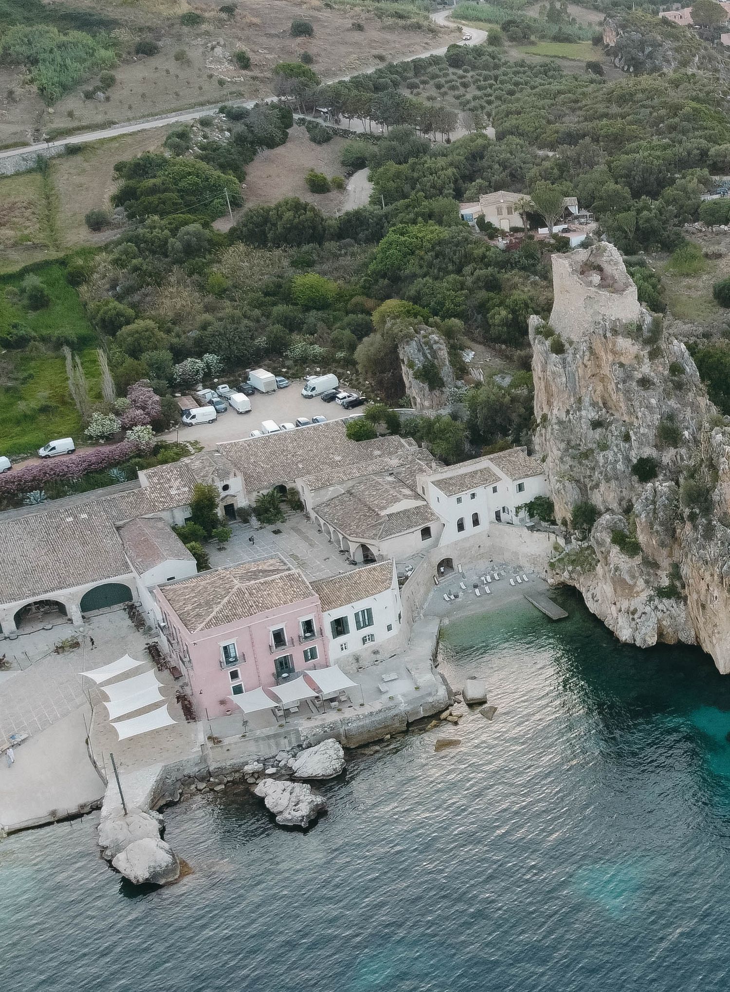 Panoramic view of a Mediterranean fishing village with white buildings and pink accents along rocky shores.