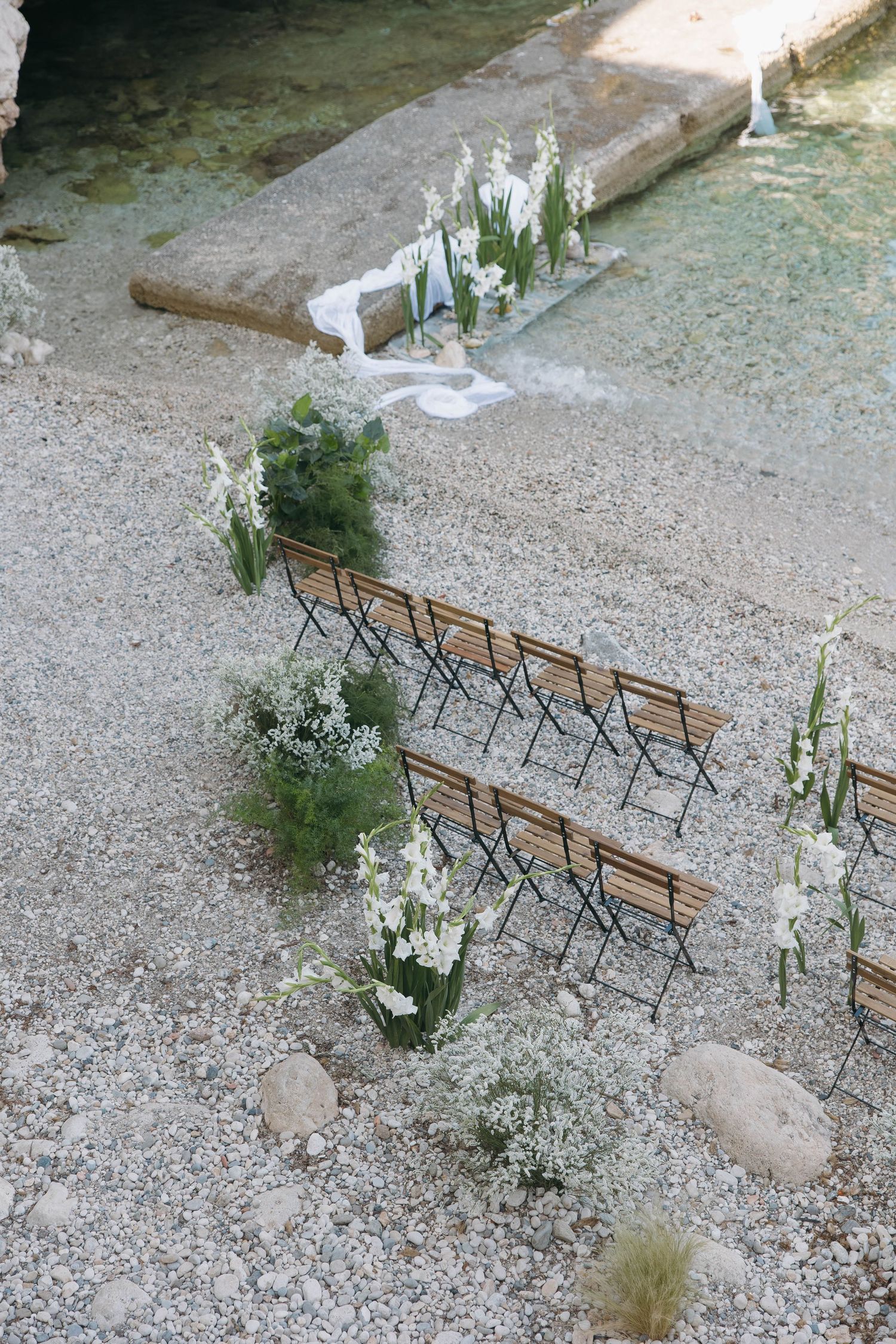 White floral decorations and wooden chairs arranged on gravel for an outdoor ceremony.