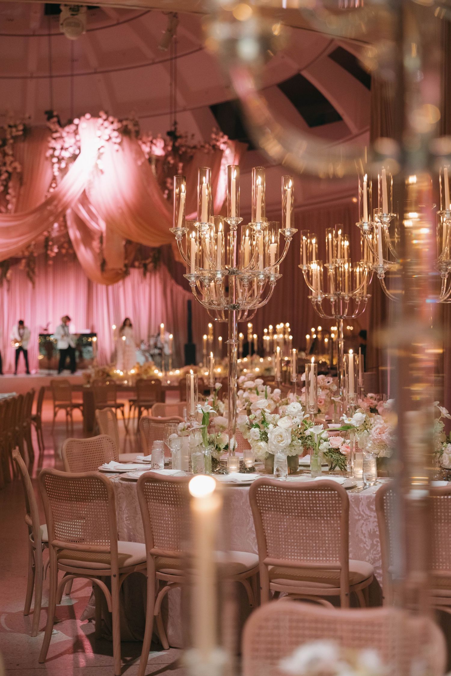 Elegant wedding reception tables adorned with tall candelabras and floral centerpieces in a pink-lit ballroom setting.