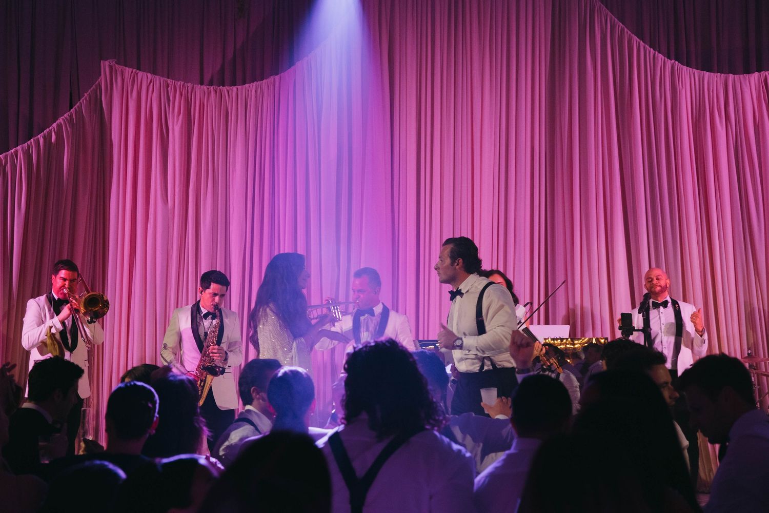 Band performs on stage with dramatic purple lighting and white curtain backdrop.