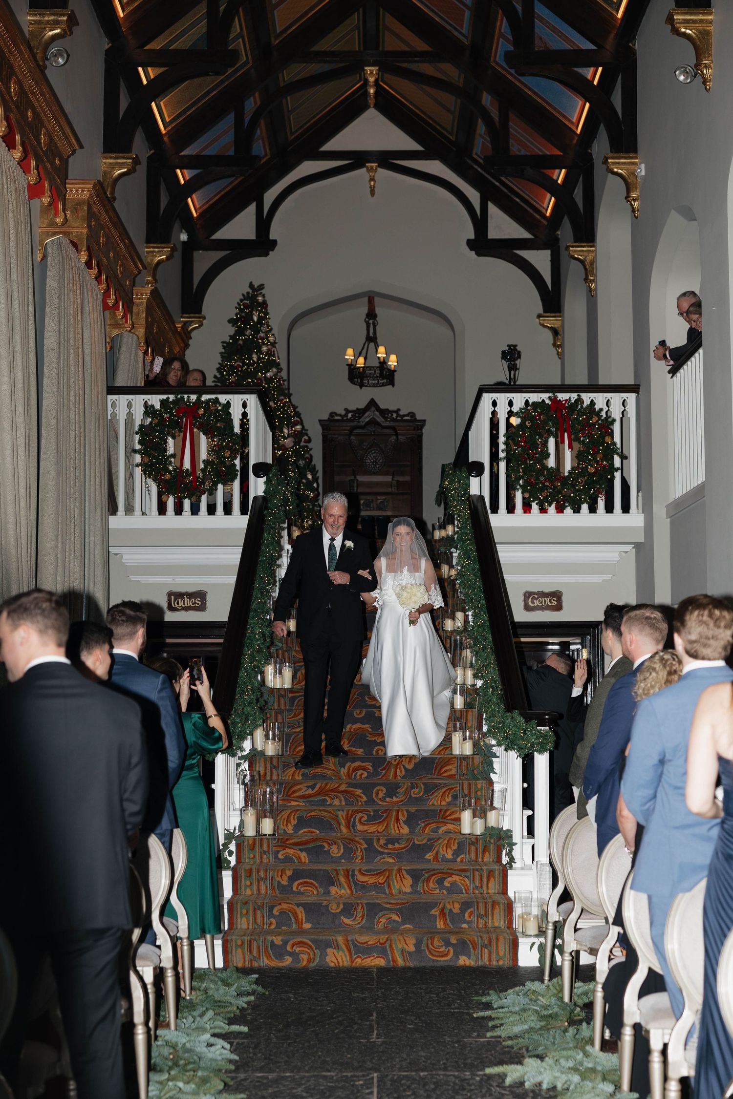 Wedding ceremony setup in a grand hall with vaulted wooden ceiling and holiday decorations.