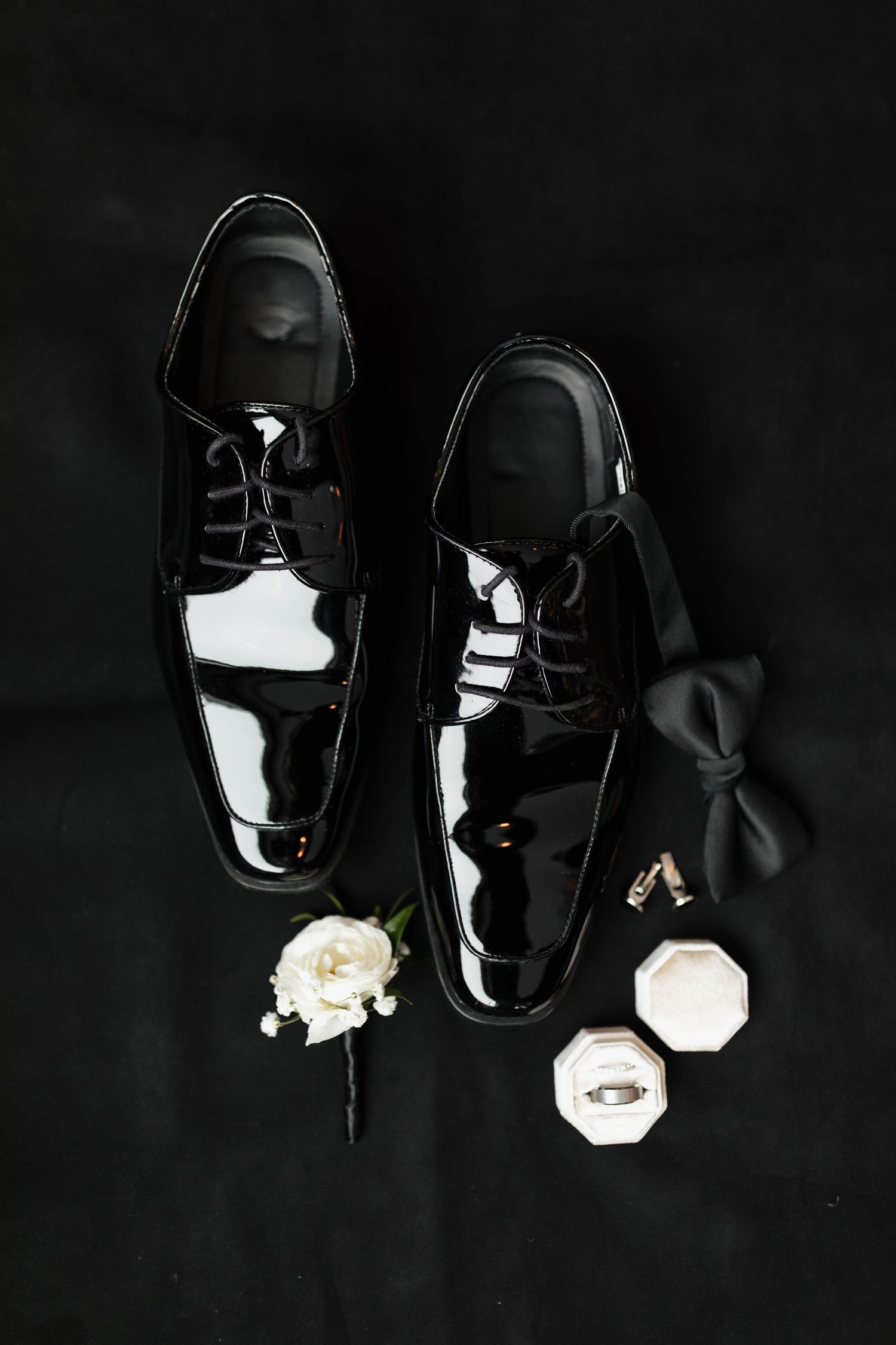 Artistic overhead view of black formal shoes with white floral accents on dark background.