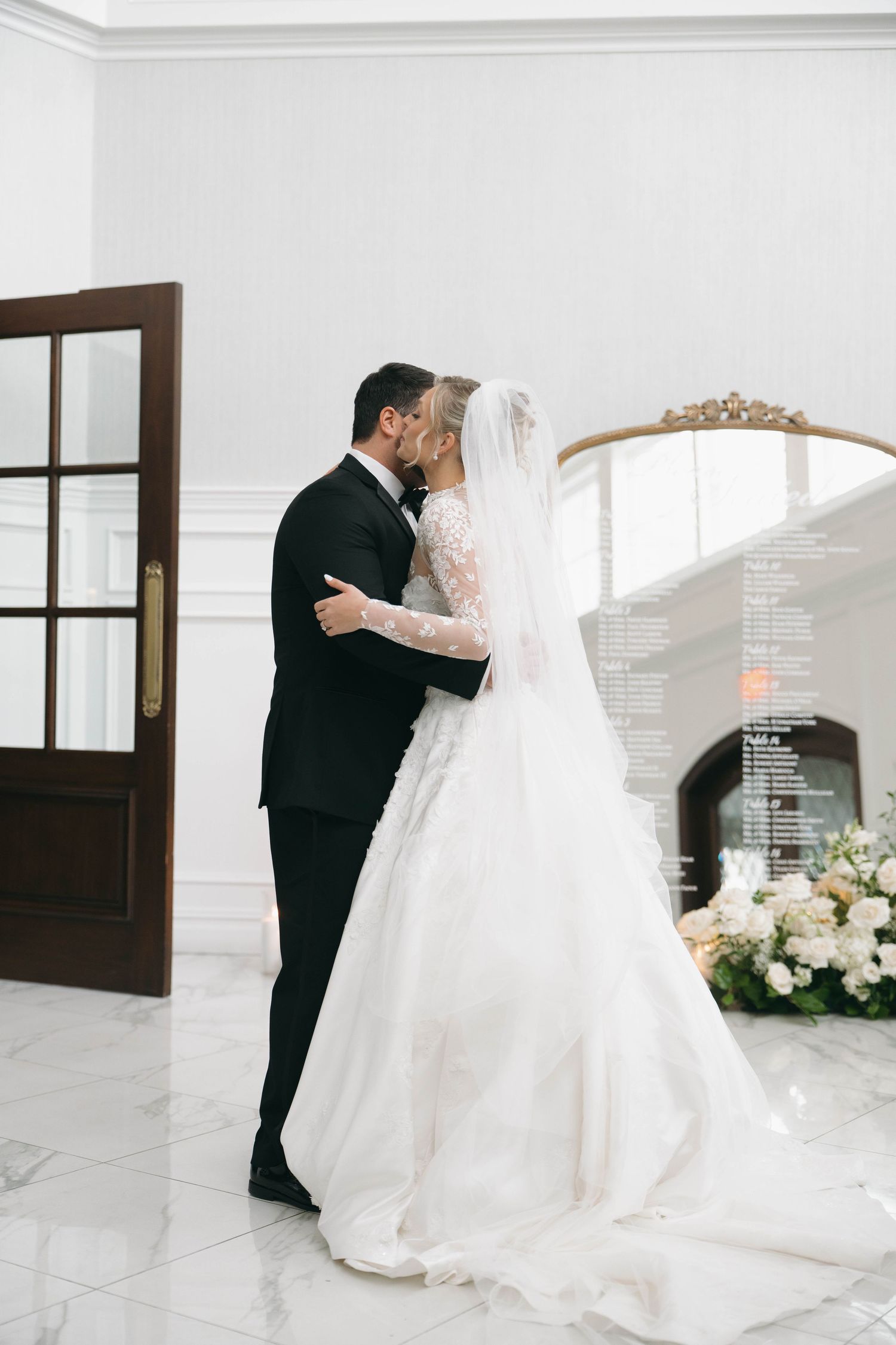 A romantic wedding moment captured in an elegant white interior with floral decorations.
