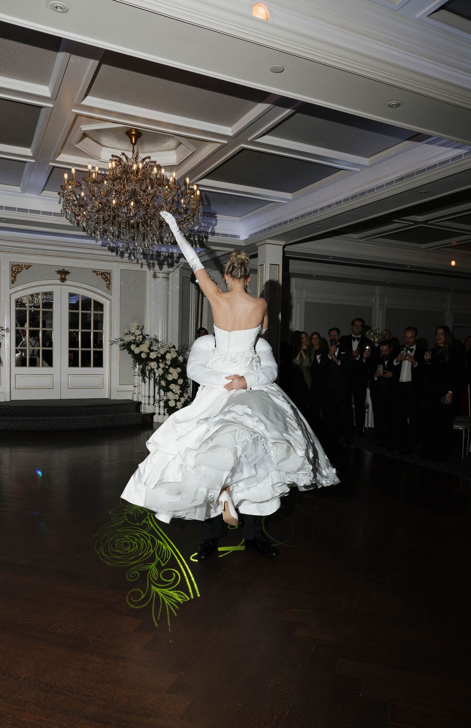 Wedding couple performs dramatic dance lift in elegant ballroom setting.
