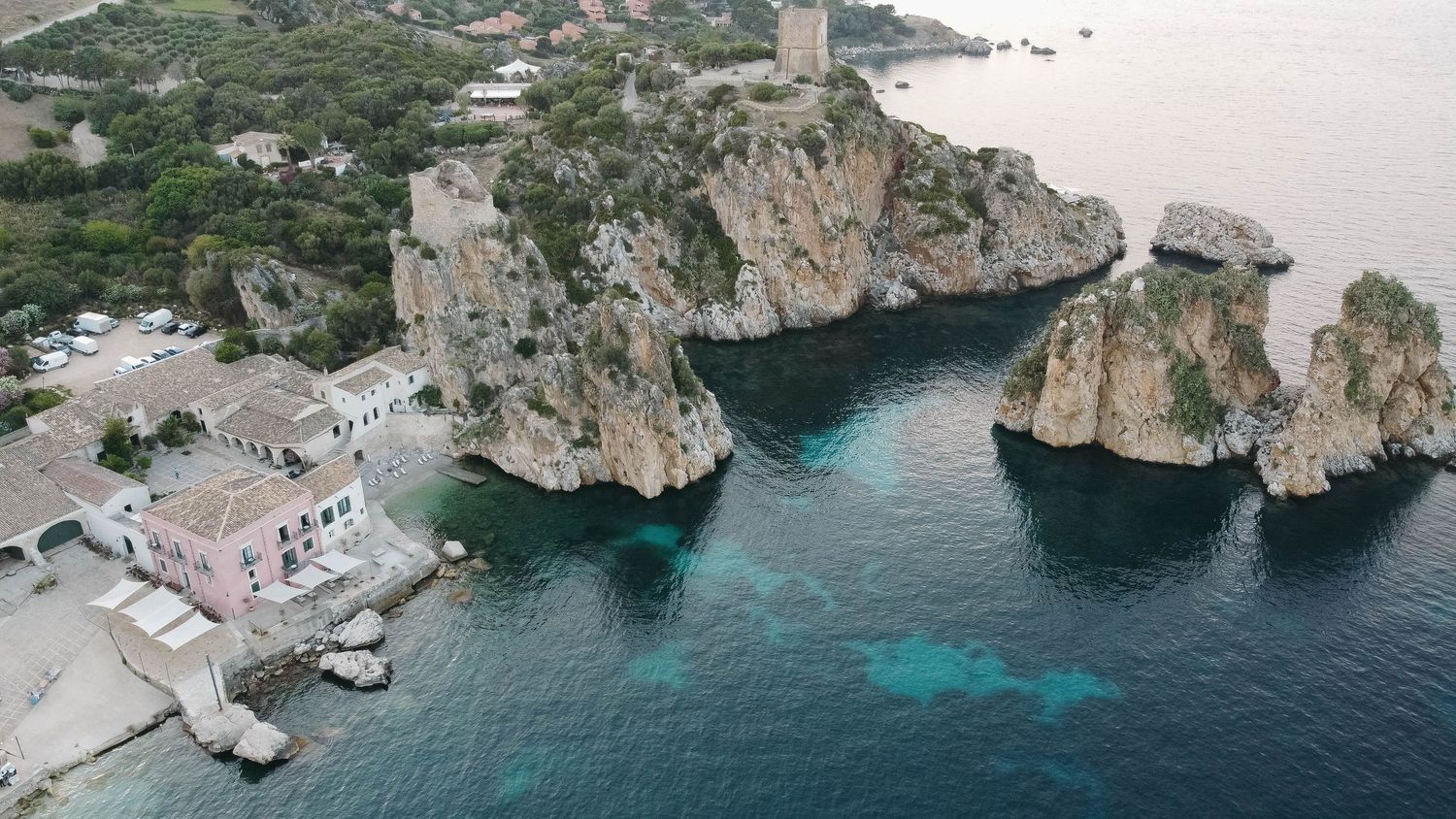 Bird's eye view of a secluded coastal cove with crystal clear waters and rugged cliffs.