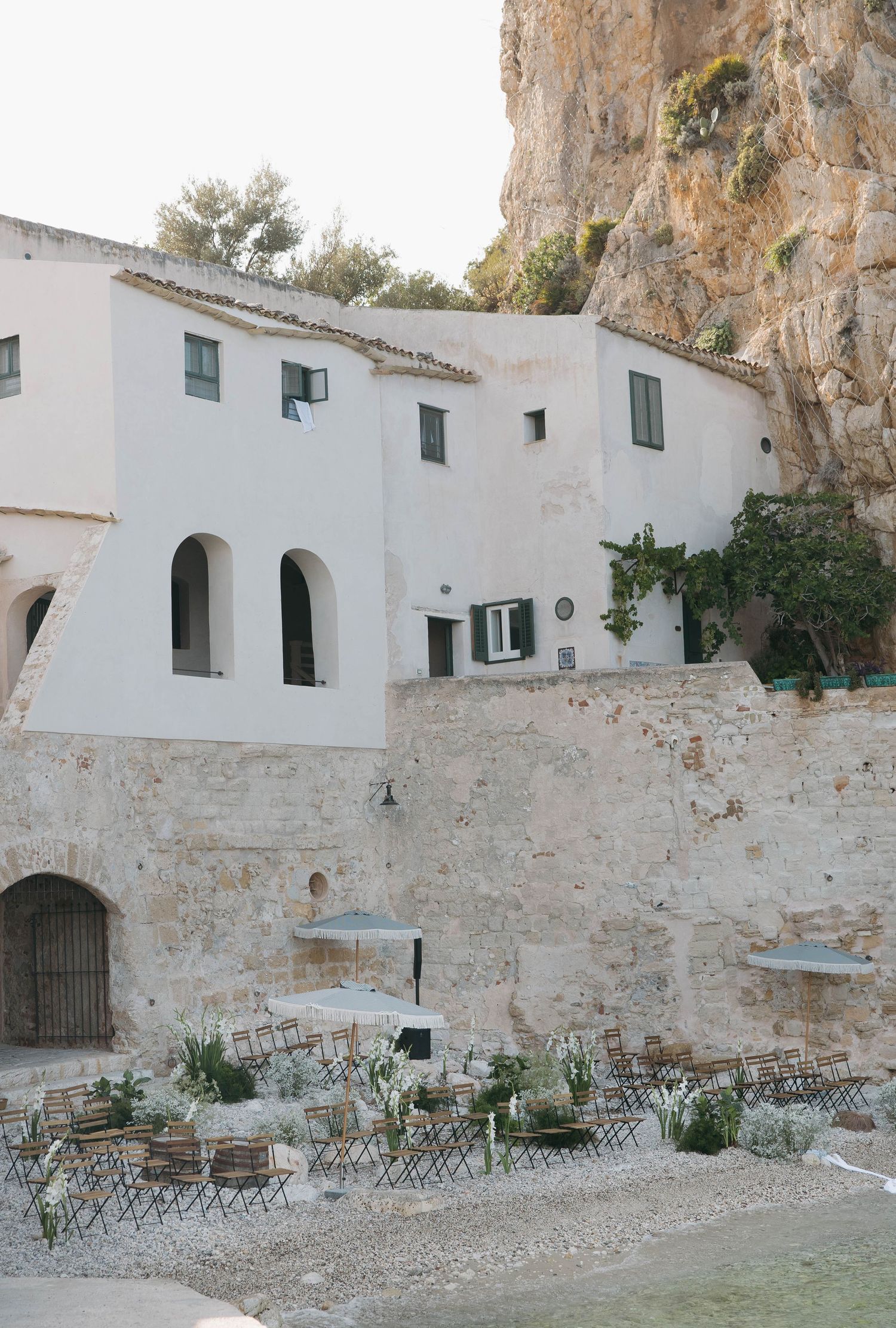 Ancient white stone buildings with green shutters built into dramatic coastal cliffs.