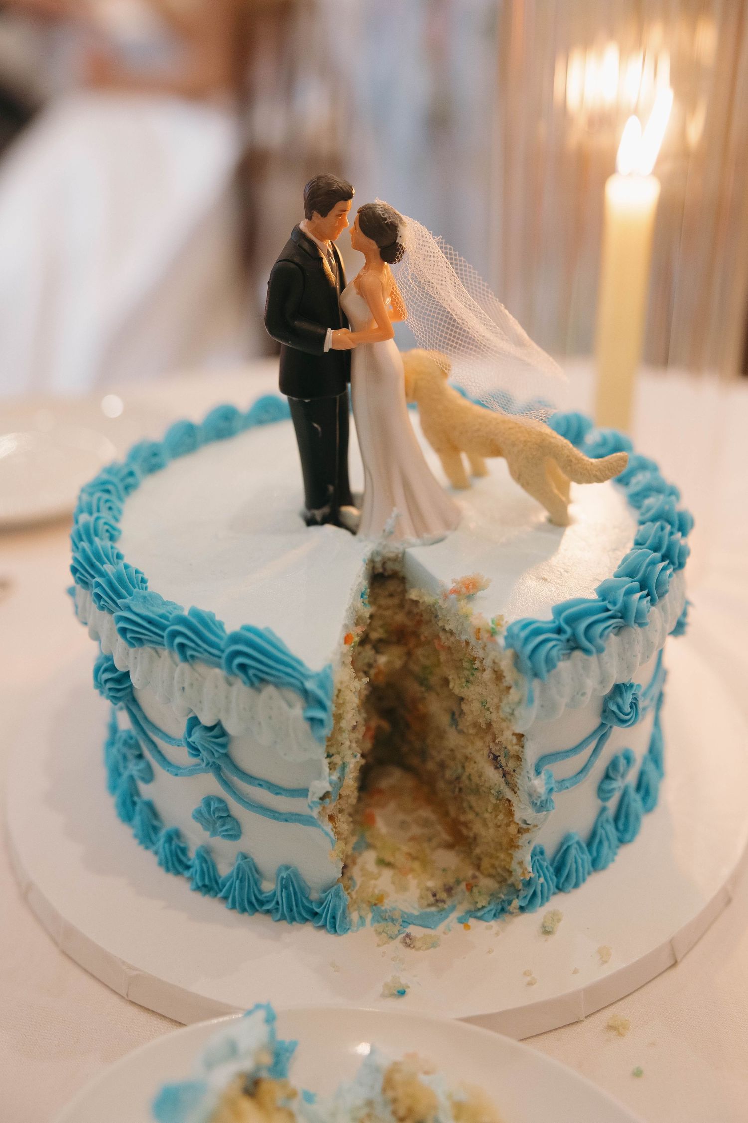 Wedding cake with blue frosting details and bride and groom topper, showing partially eaten interior.