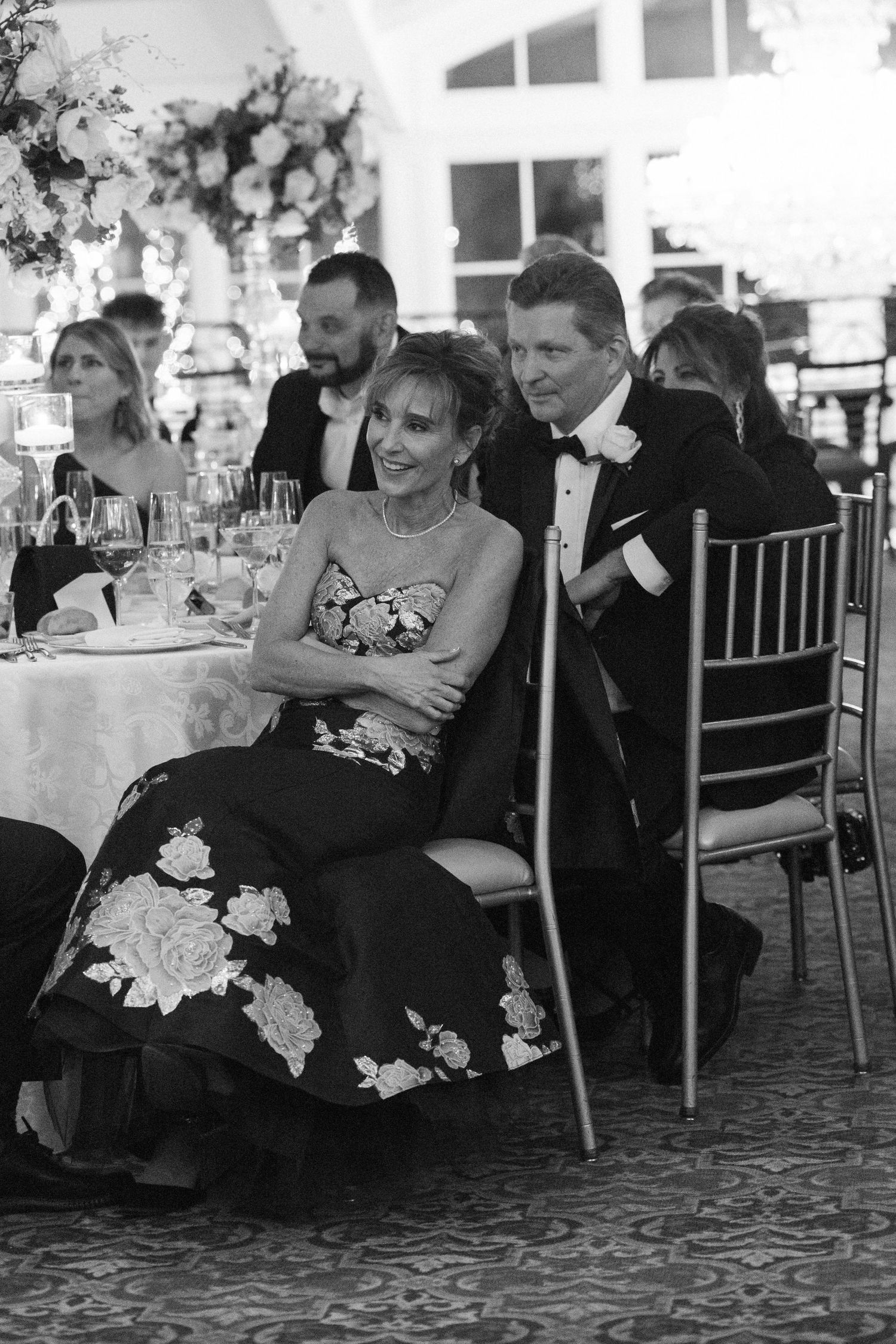 Wedding guests laugh and smile while seated at elegantly decorated reception tables.