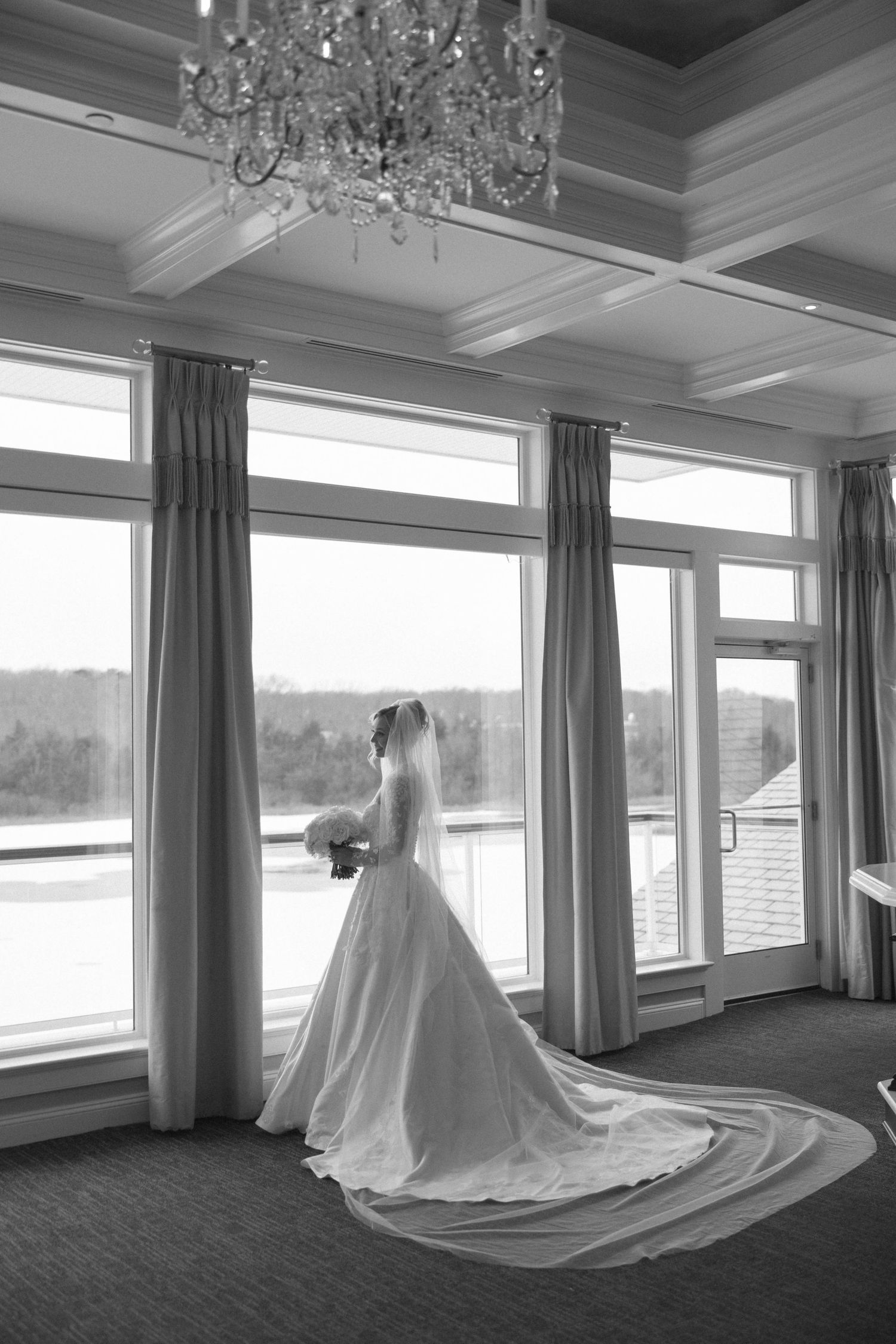 Black and white wedding dress portrait in elegant room with large windows and chandelier.