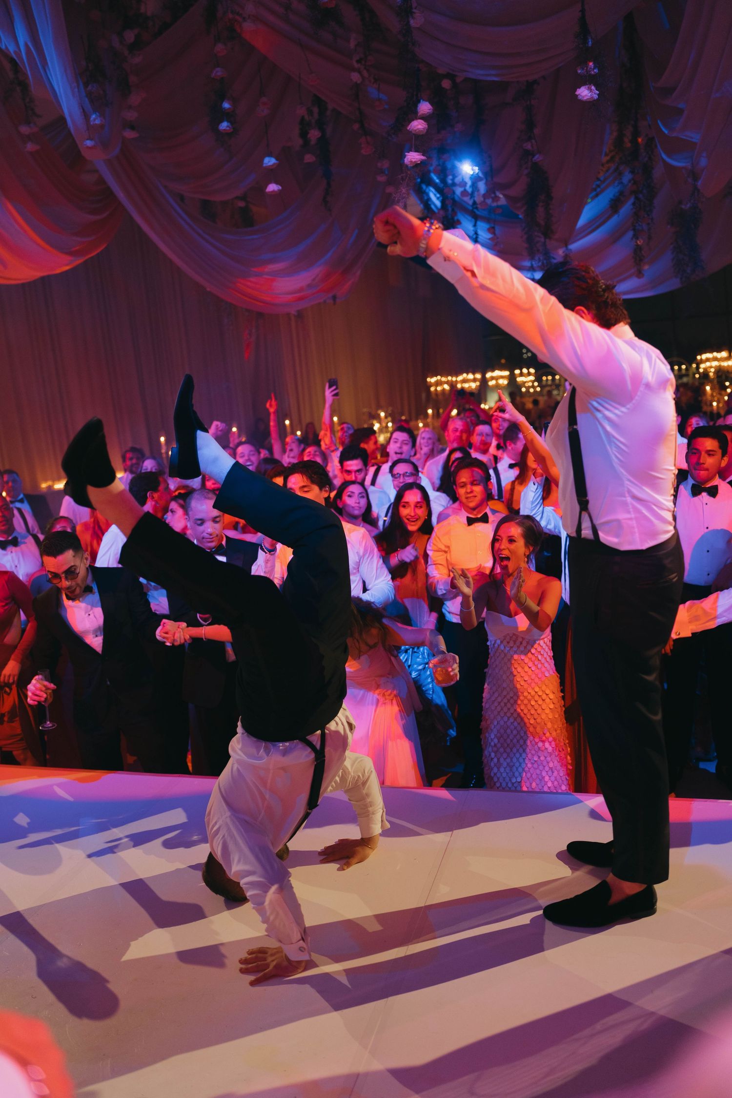 Wedding guests performing synchronized dance moves under dramatic blue and red lighting.