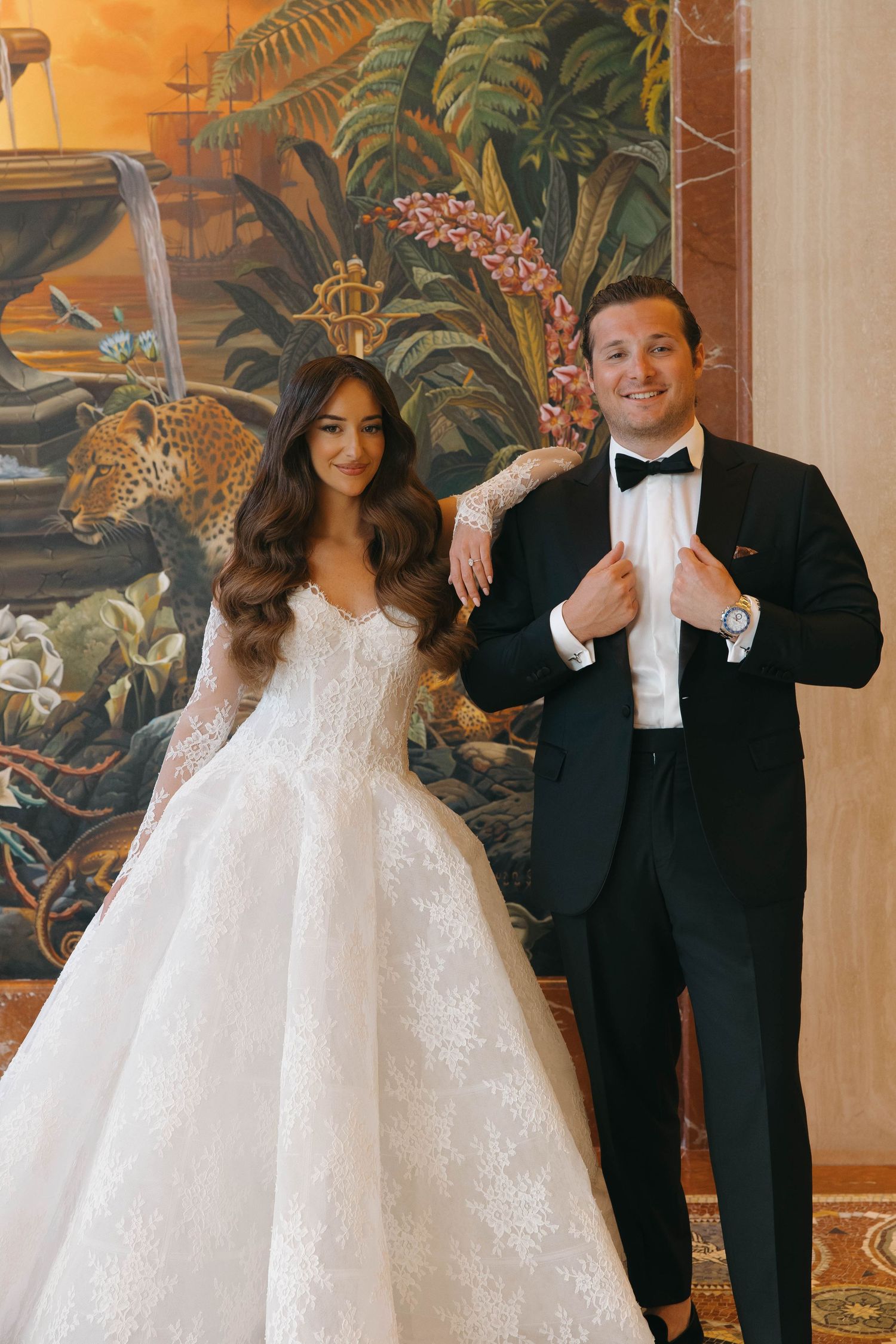 Couple in wedding attire poses playfully against a backdrop of exotic painted murals.